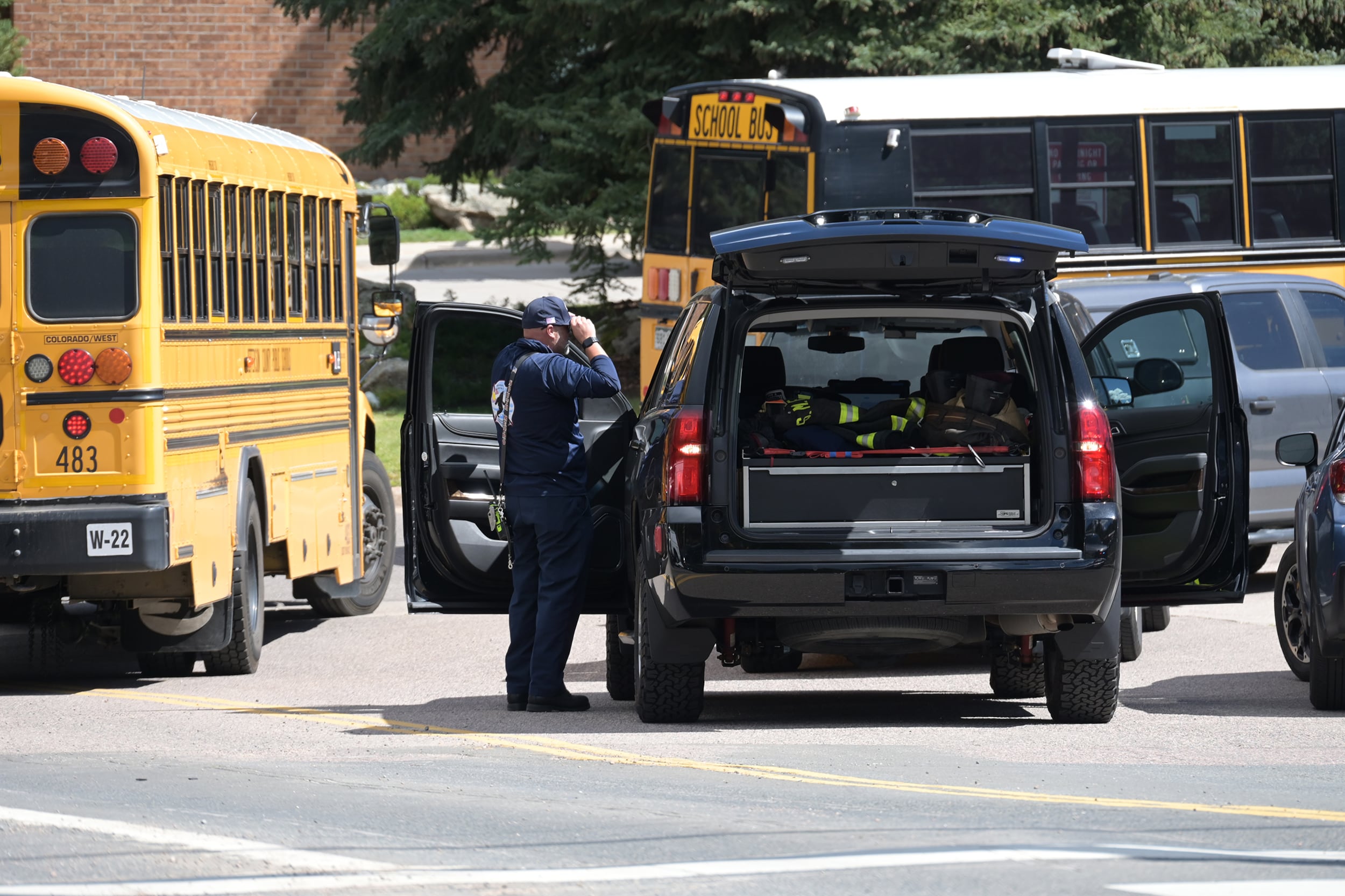 A photograph of a police office standing next to a police SUV with two yellow school busses in the background.