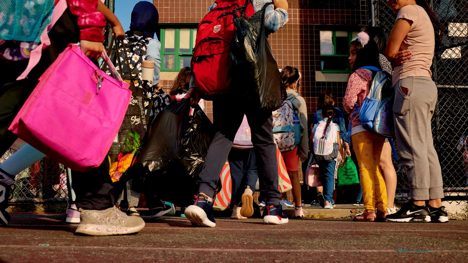 A view of children and book bags from the middle of their bodies down.