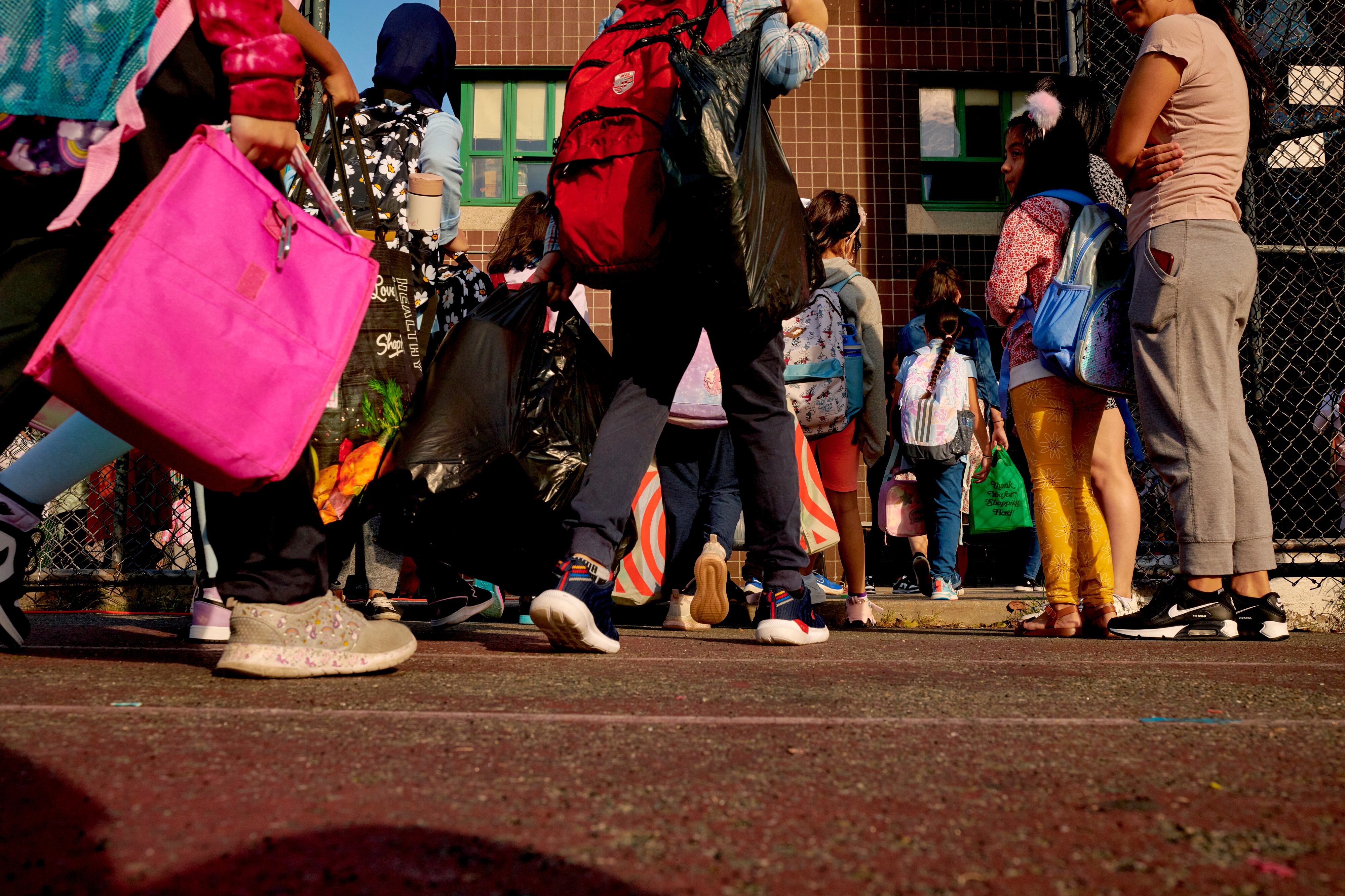 A view of children and book bags from the middle of their bodies down.