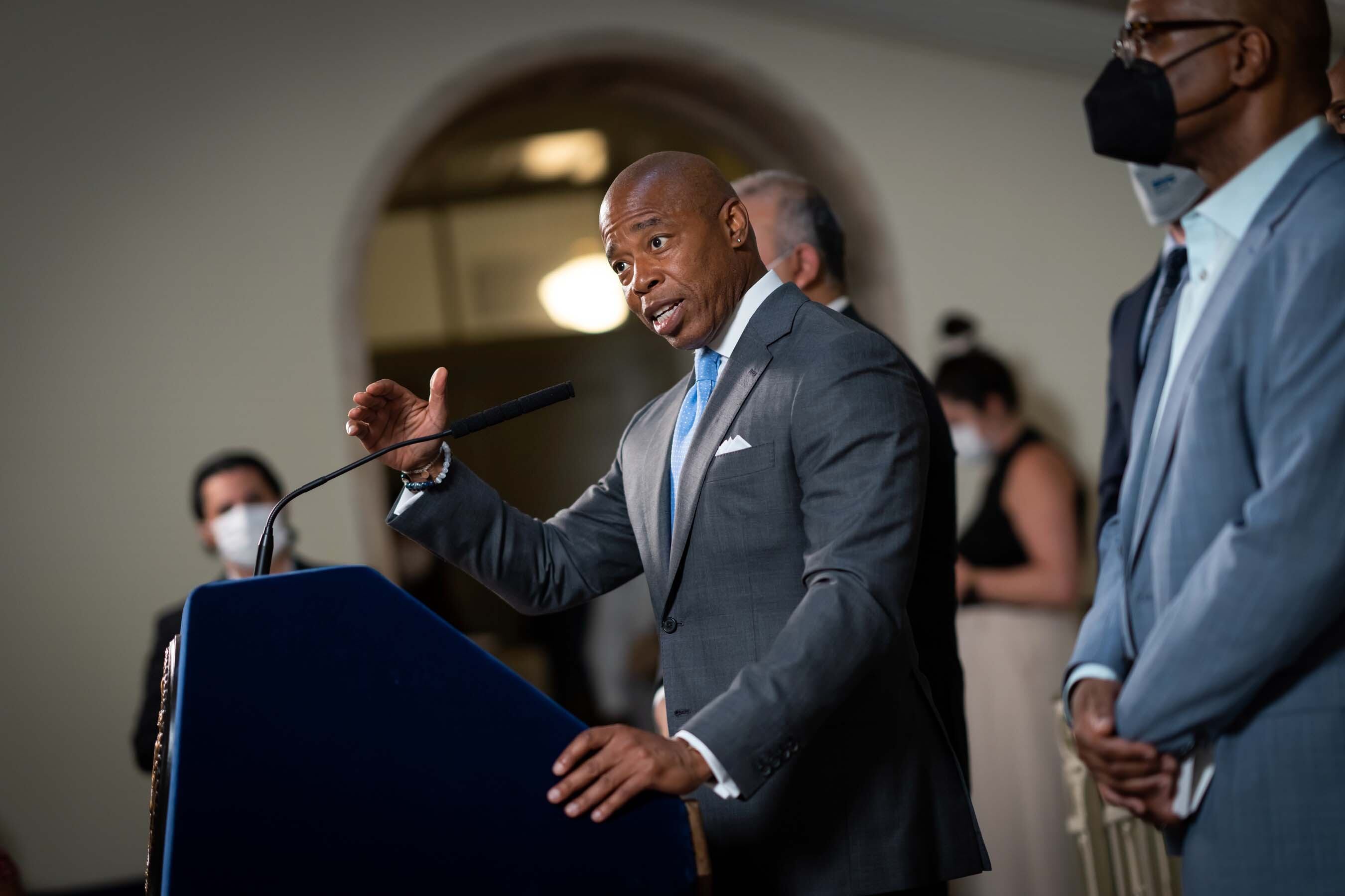 A man in a gray suit stands and speaks at a lectern.