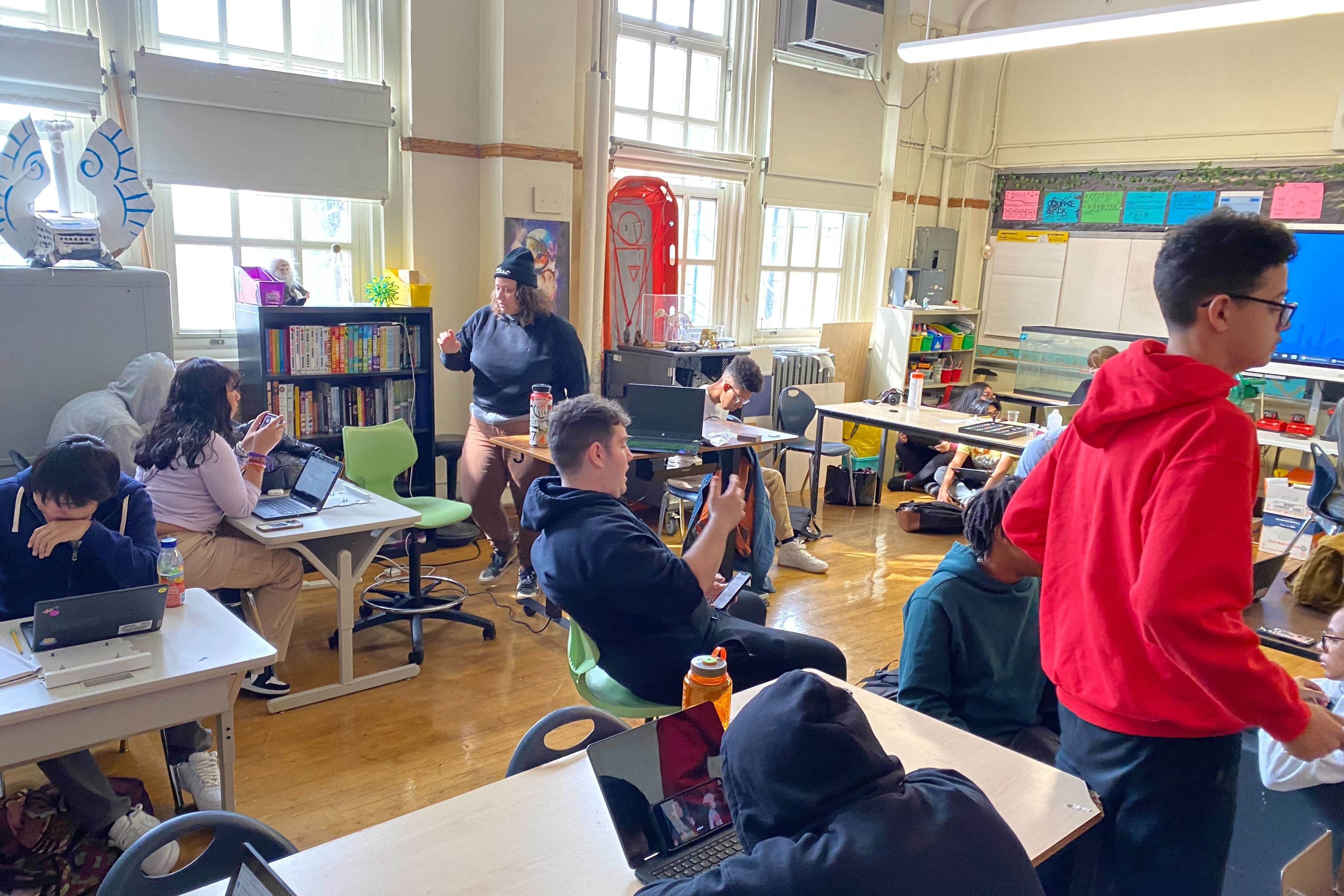 Teens sit at tables scattered around a classroom working on different projects.