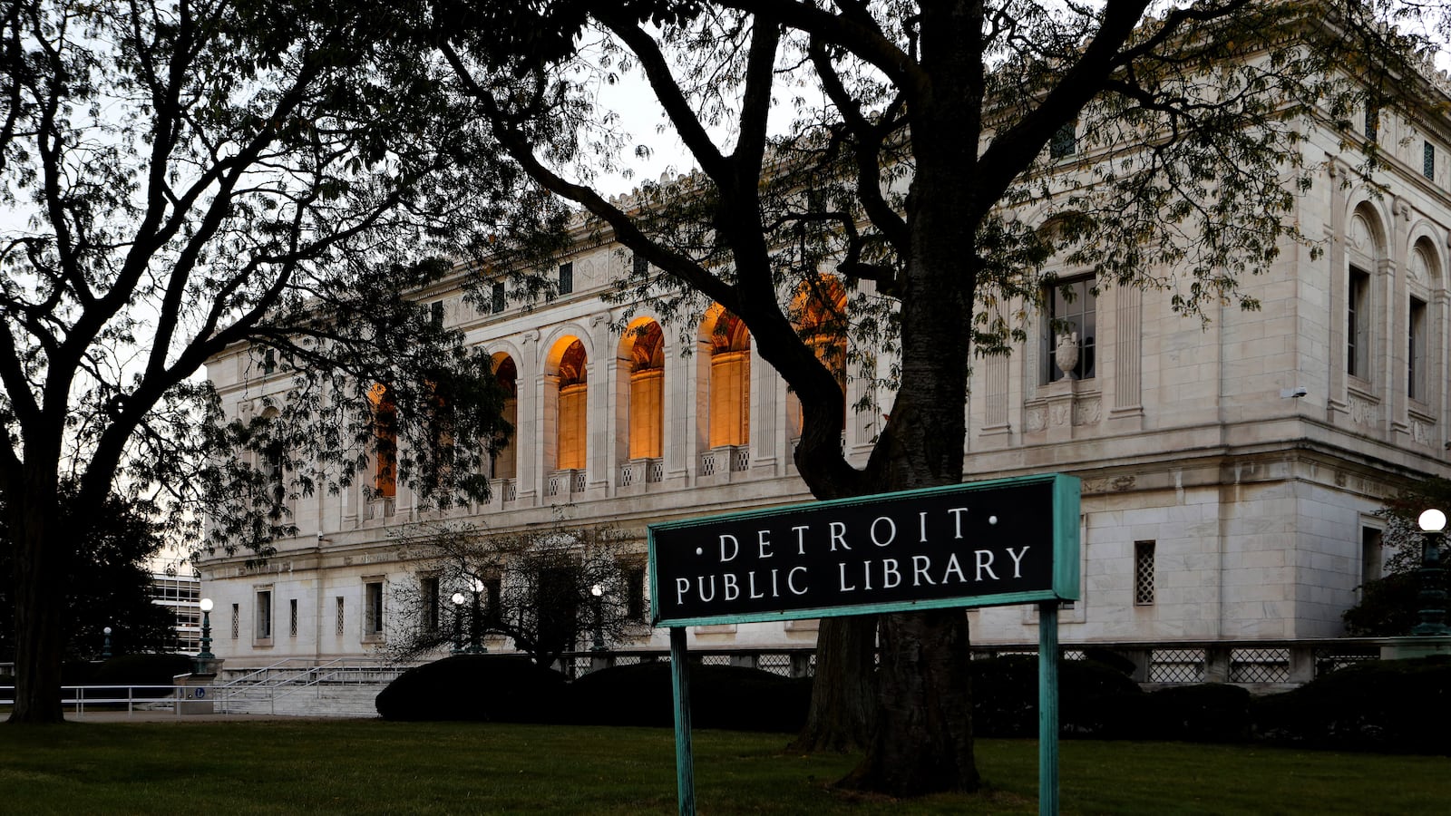 Photo of an Italian Renaissance building. In the foreground are trees and a sign reading "Detroit Public Library."