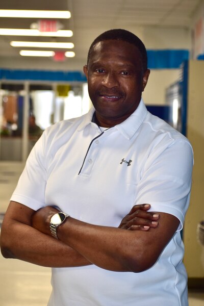 A smiling man stands with his arms crossed. He is wearing a white polo shirt.