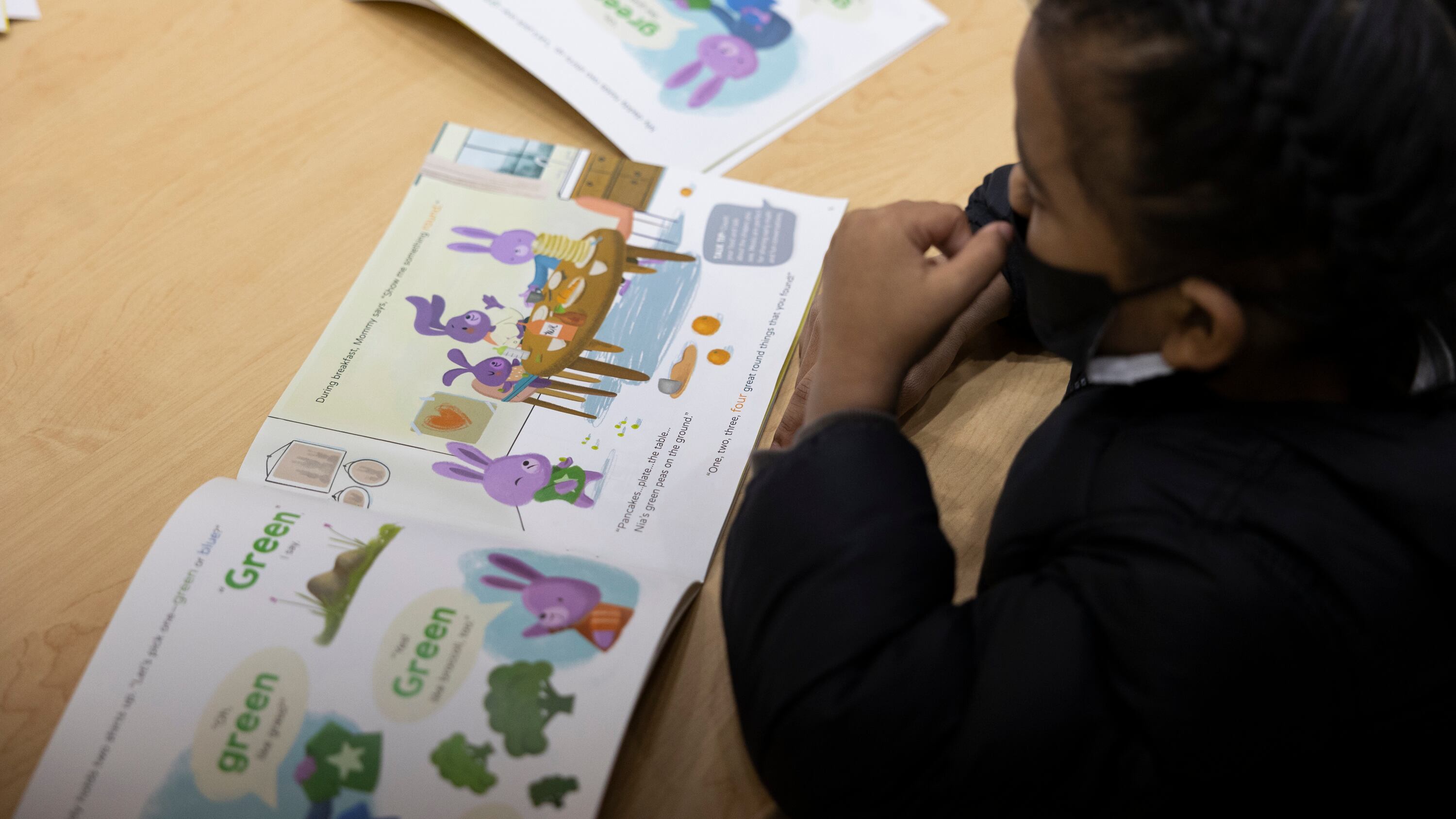 A little boy reads a children’s book at a small wooden table.