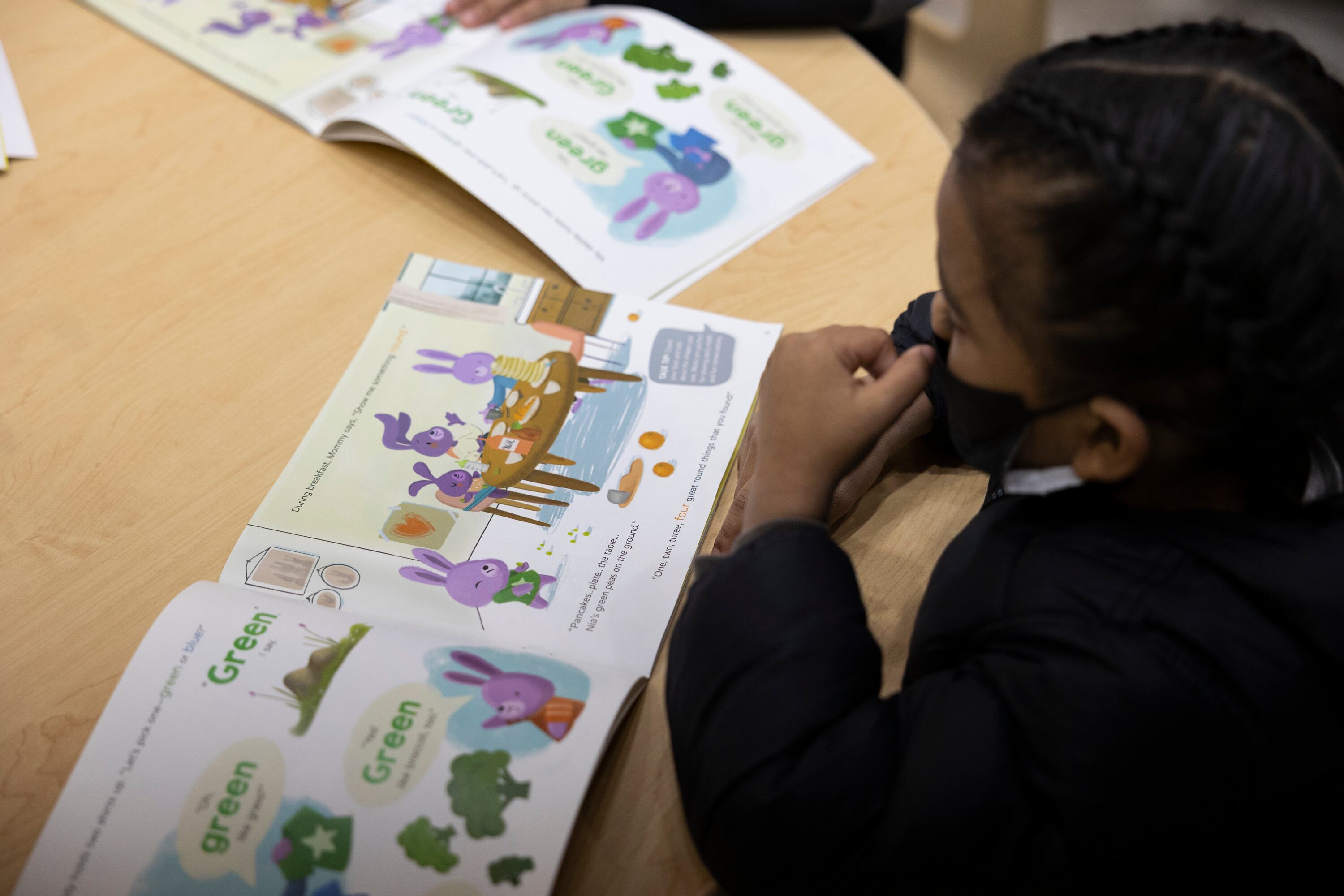 A little boy reads a children’s book at a small wooden table.