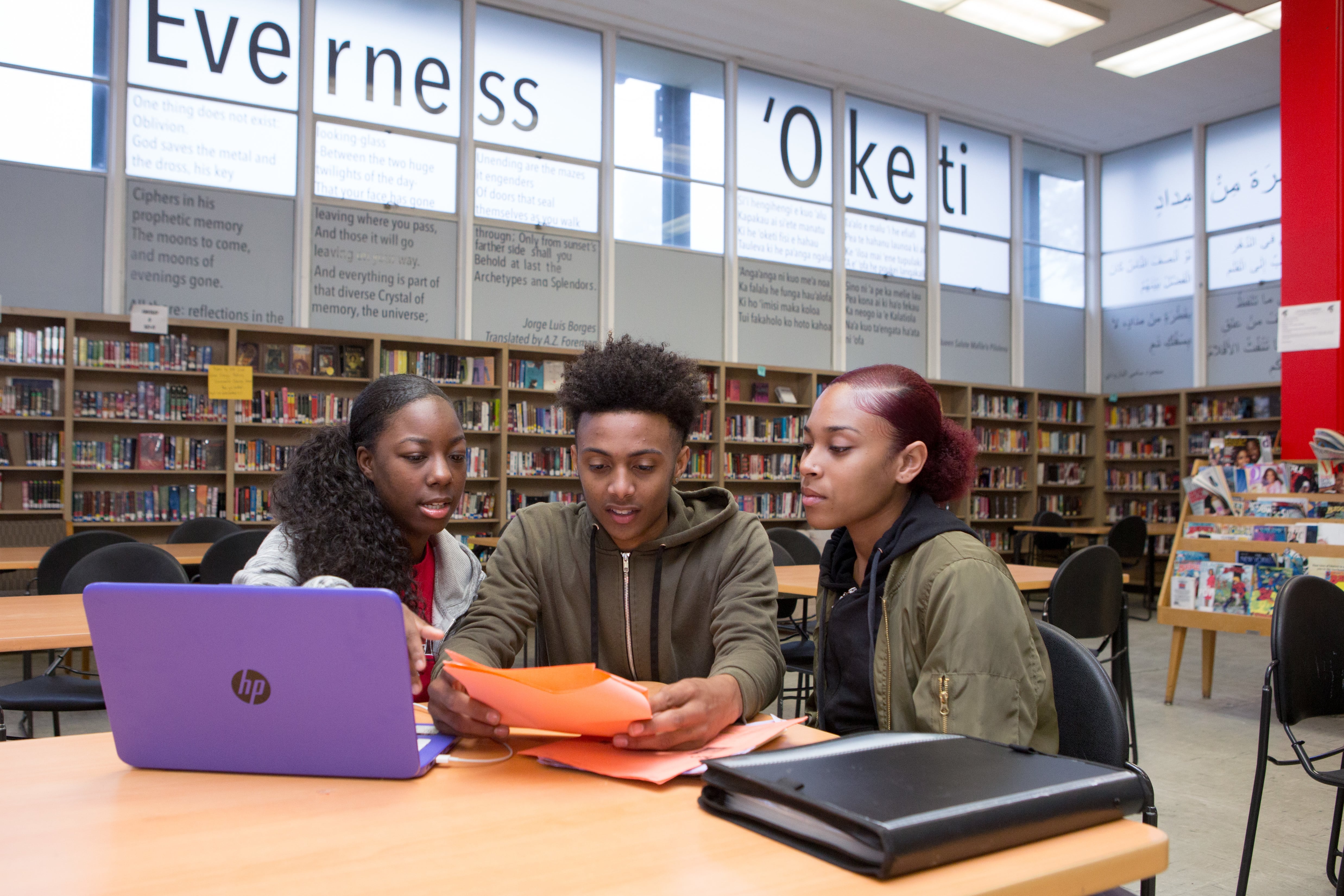 Three students sitting together at a table in a library.