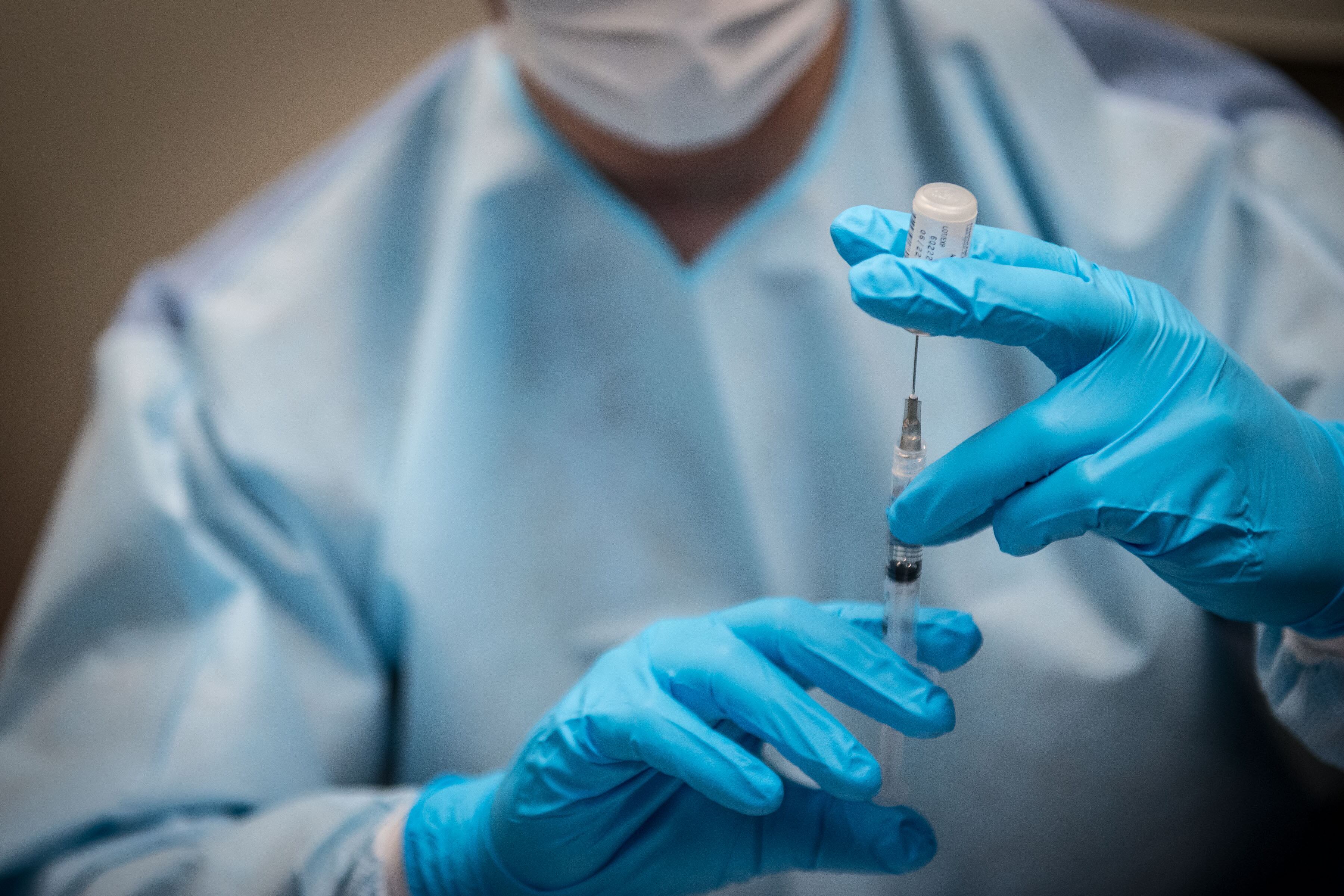 A medical worker prepares a dose of a COVID vaccine, wearing full protective gear.
