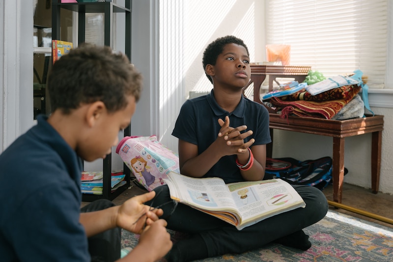 Two young boys sit on the floor, one is holding a book.