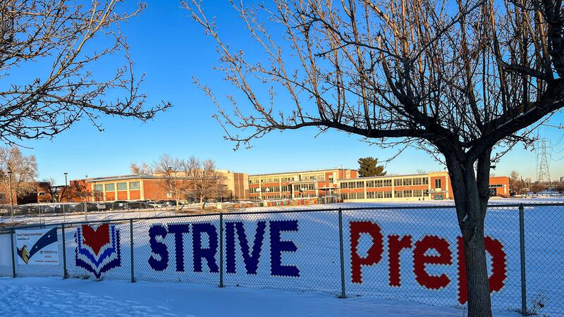 A fence that says “STRIVE Prep” sits in front of a school building. Snow covers the ground.