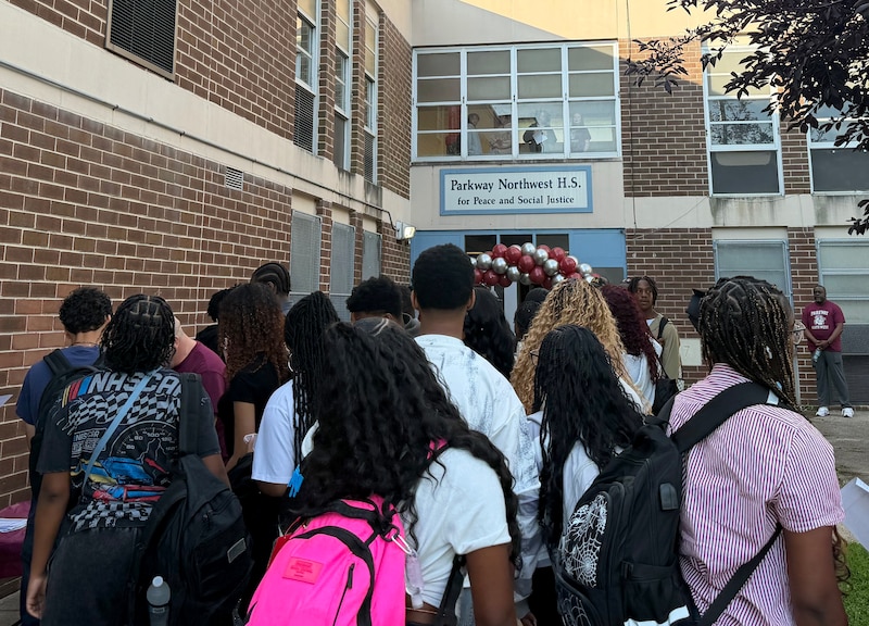 A group of Black student wearing backpacks all walk toward the front entrance of a school building.