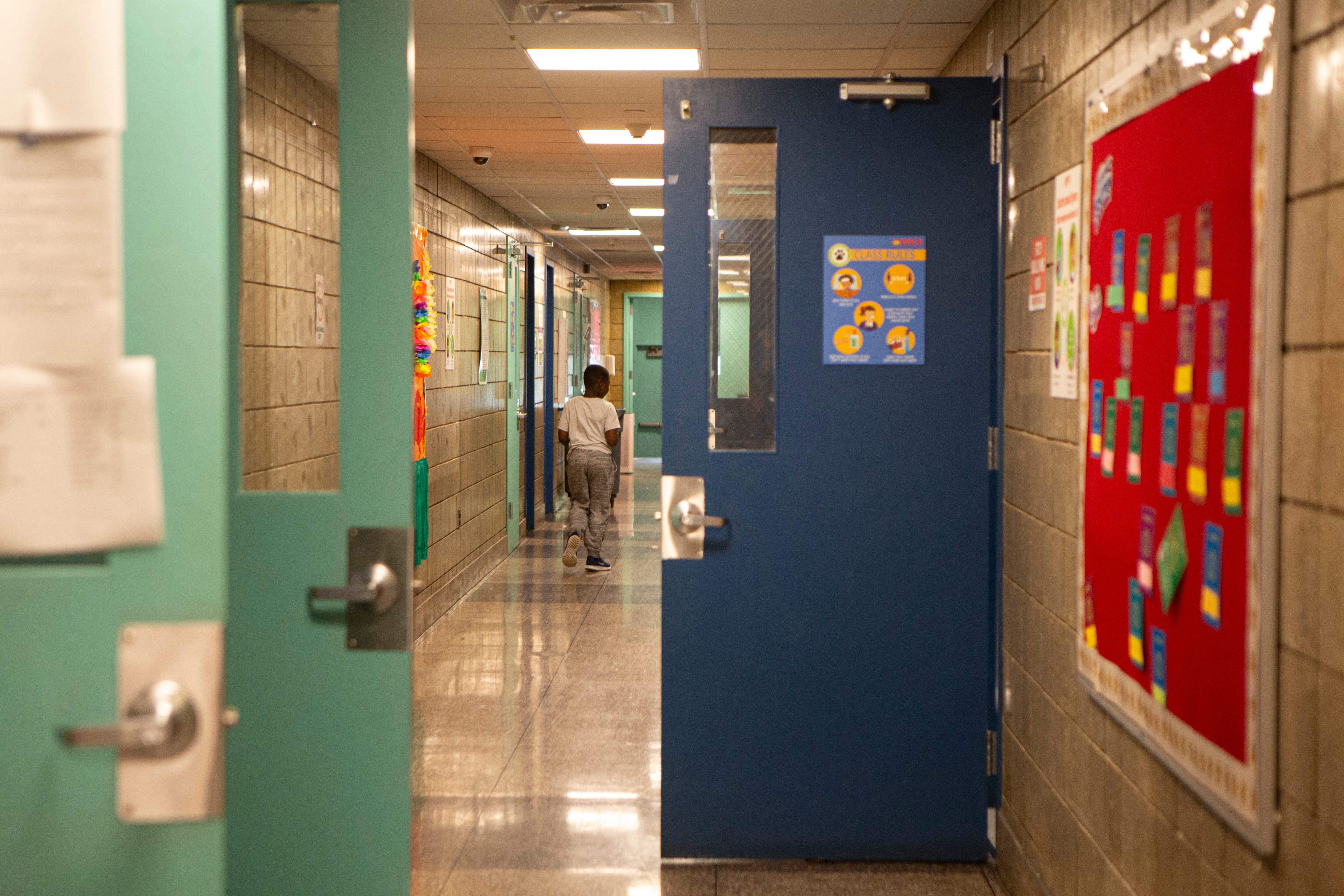 A blue classroom door and two green doors are open in the middle of a school hallway.
