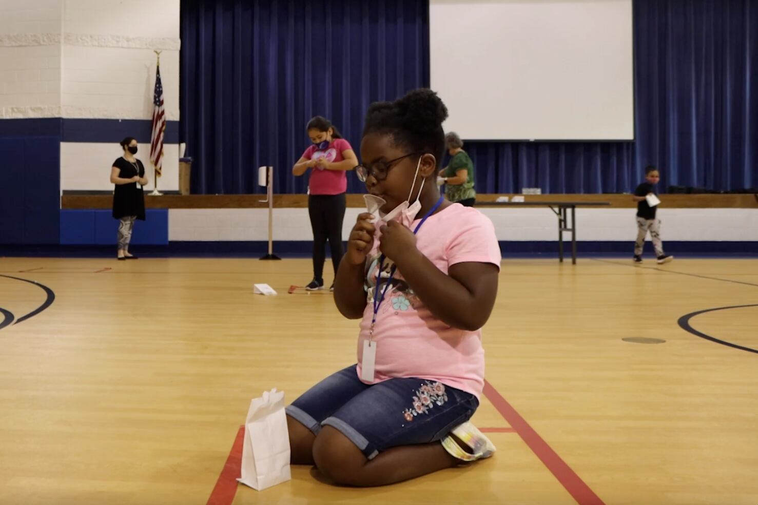 A young girl produces a saliva sample for a SHIELD COVID test inside of a large gymnasium.