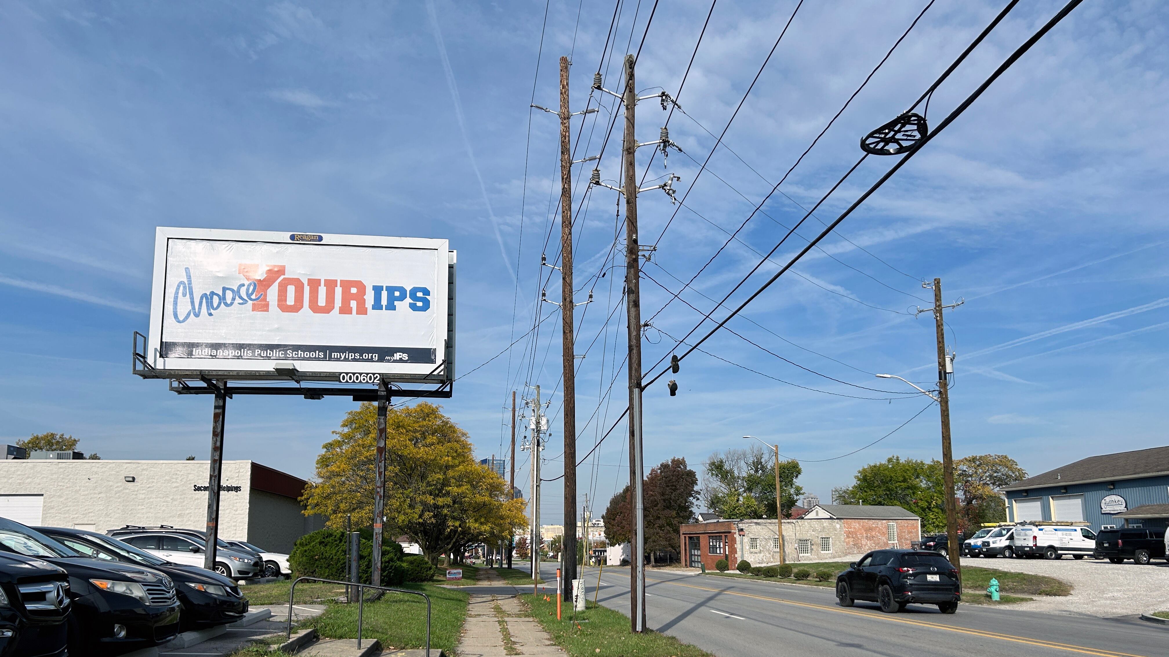 An IPS billboard stands on the side of the road with a road to the right of the sign with a blue sky as the background.