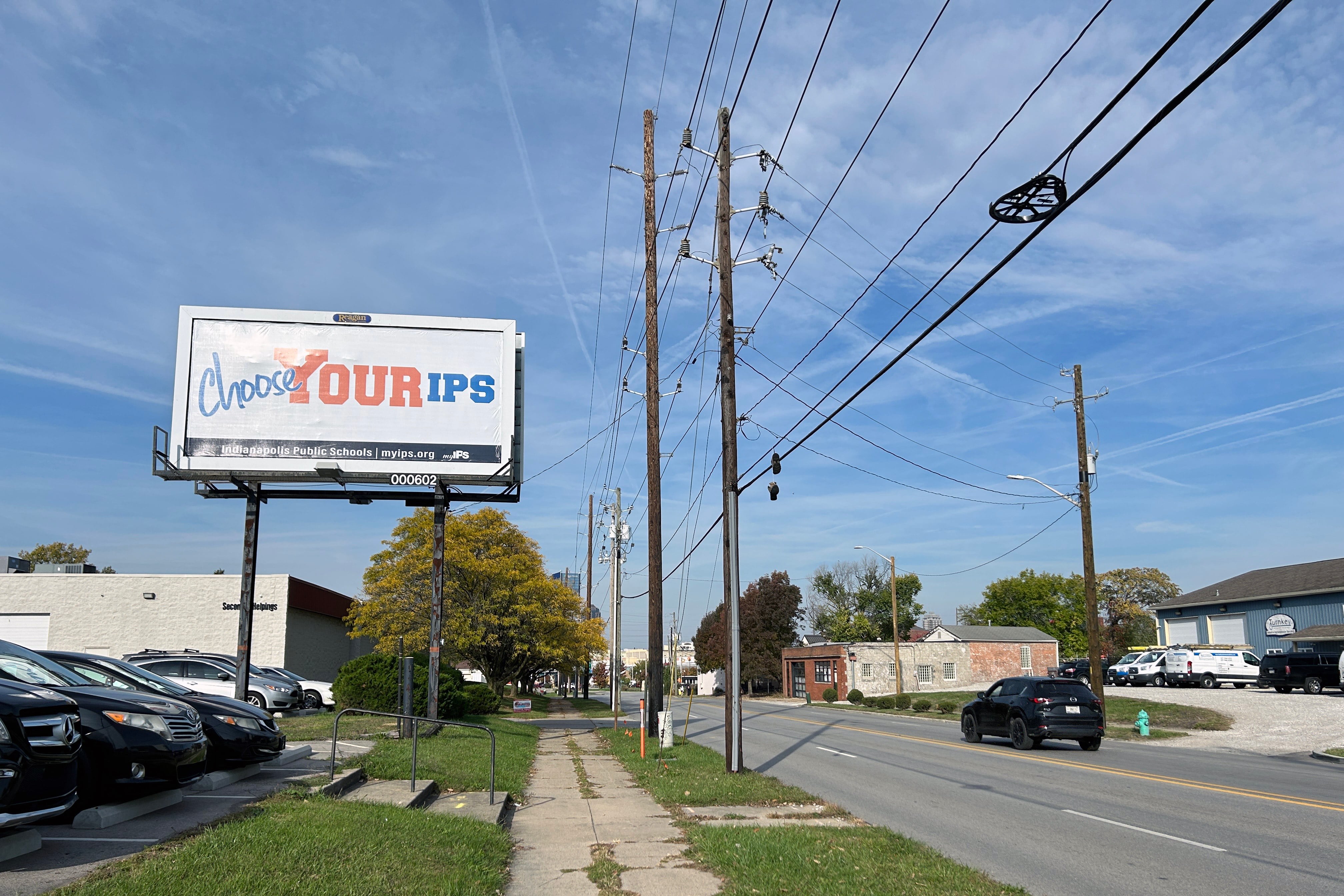 An IPS billboard stands on the side of the road with a road to the right of the sign with a blue sky as the background.