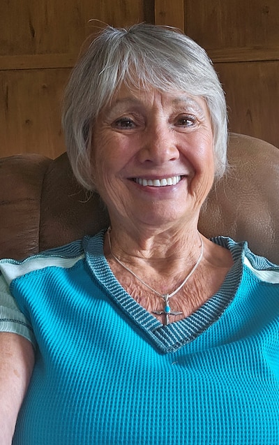 A woman with short hair and wearing a blue shirt poses for a portrait inside.