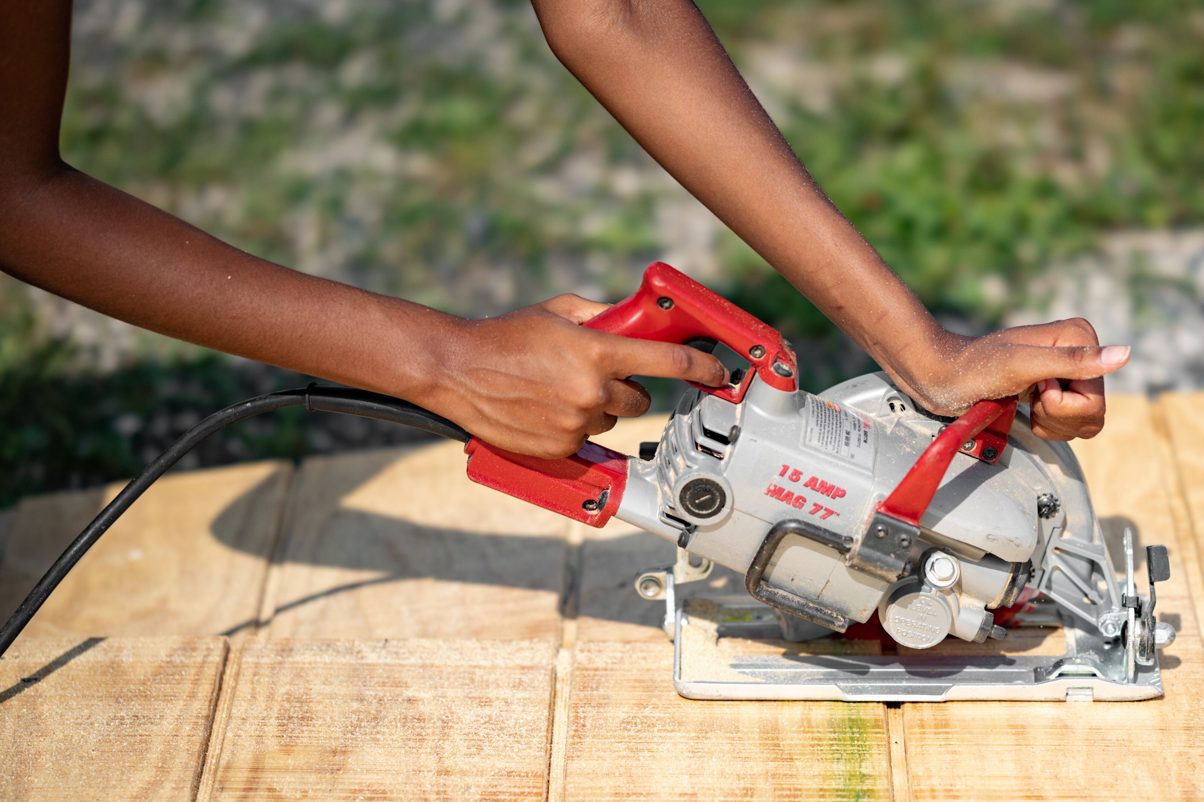 A student uses a circular saw on a piece of wood during a construction project.