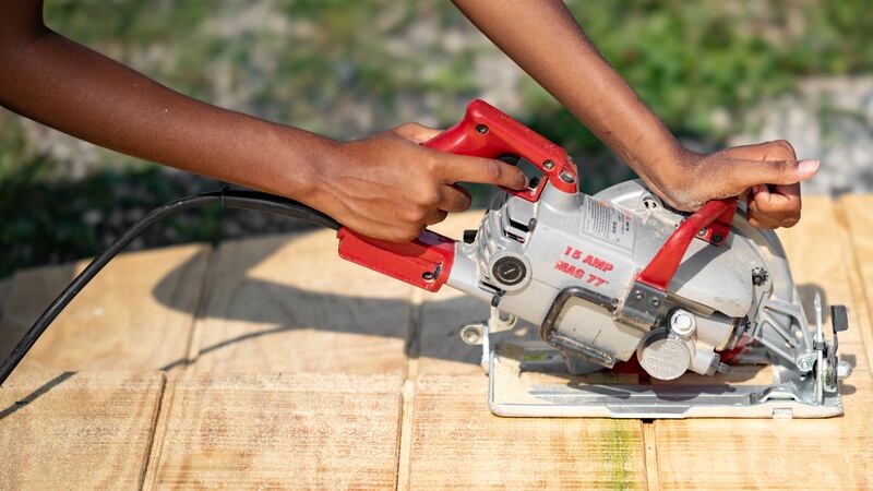 A student uses a circular saw on a piece of wood during a construction project.