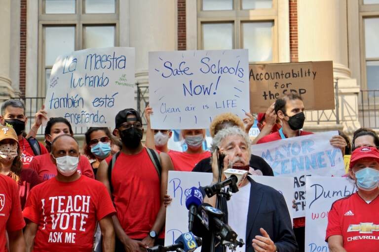 A crowd of people wearing red shirts hold signs with different writing during a protest.