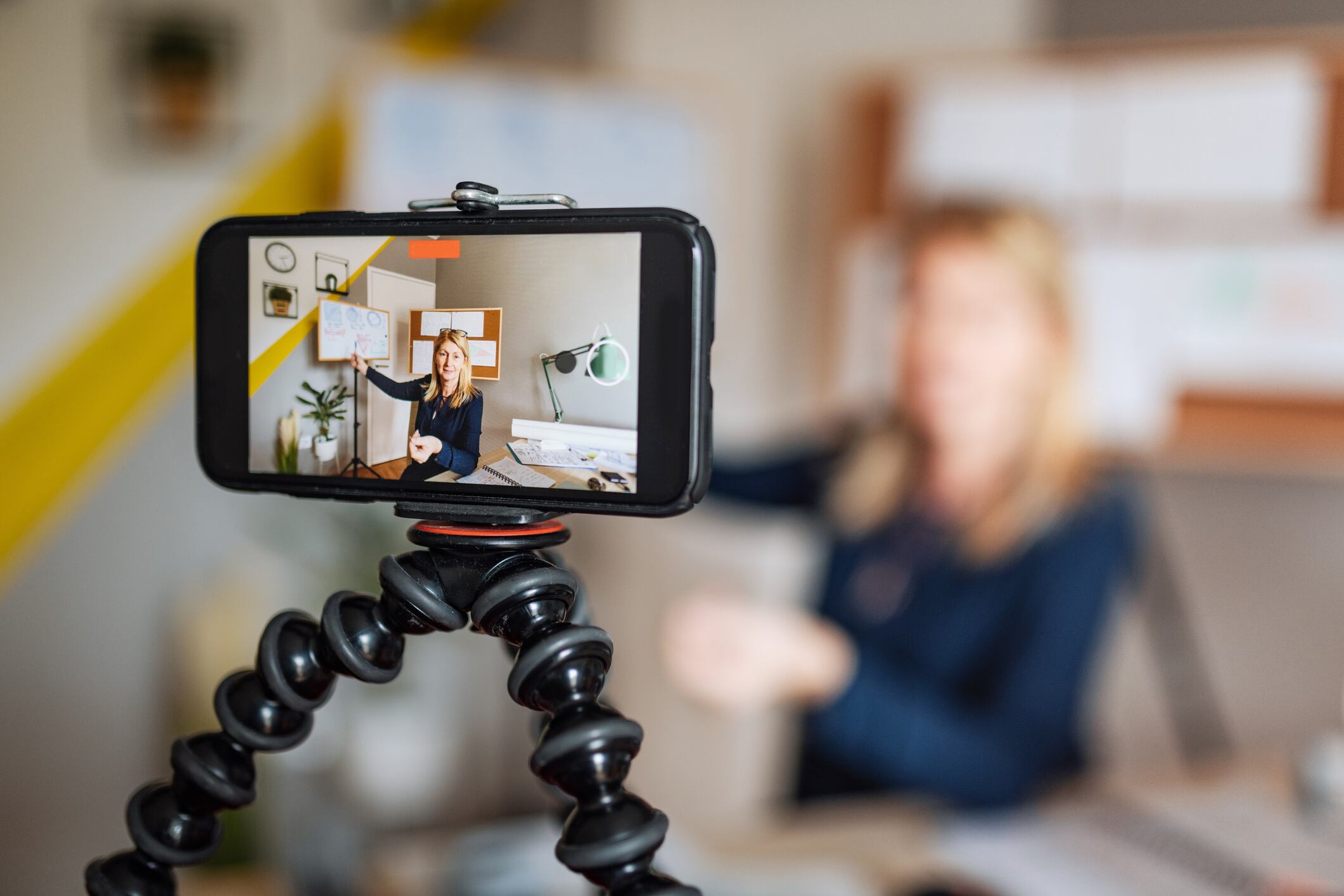 A cell phone on a stand recording a teacher during a remote learning lesson.