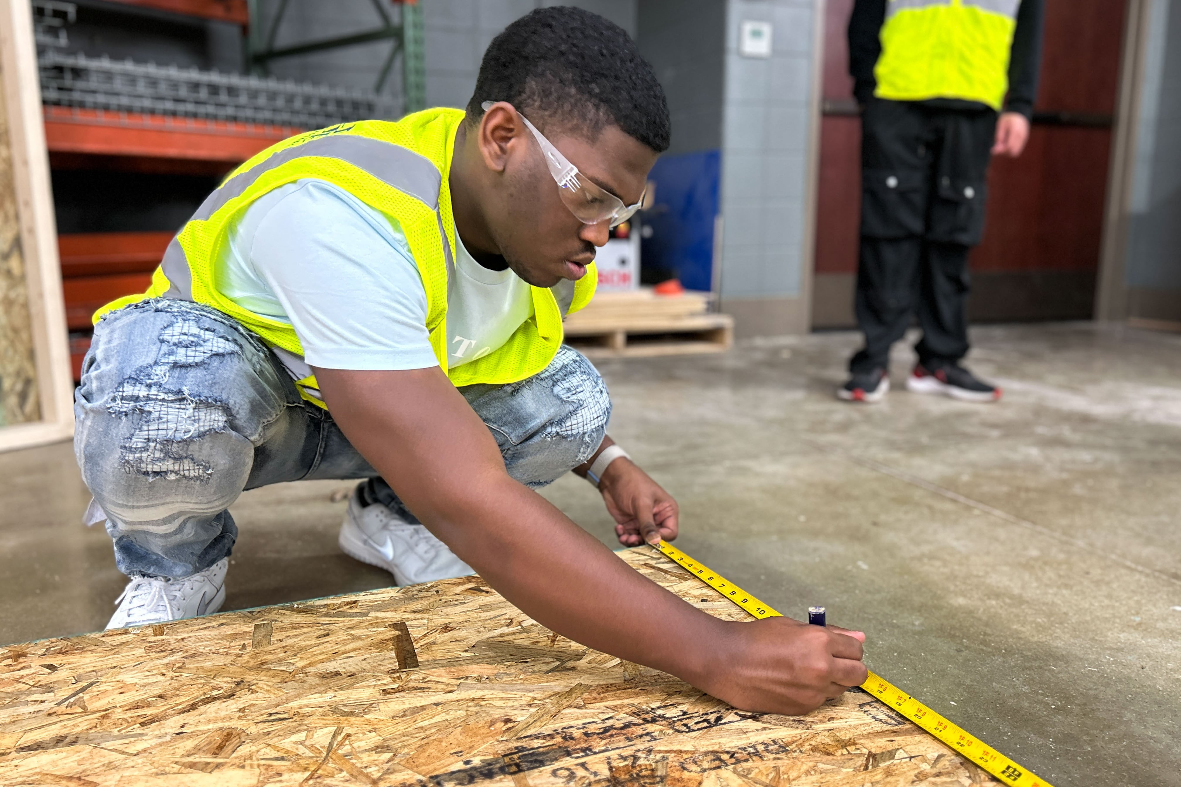 A male student with safety glasses works on a wooden board.