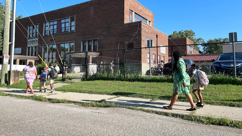 Five people walk on a sidewalk heading into a brick school building.