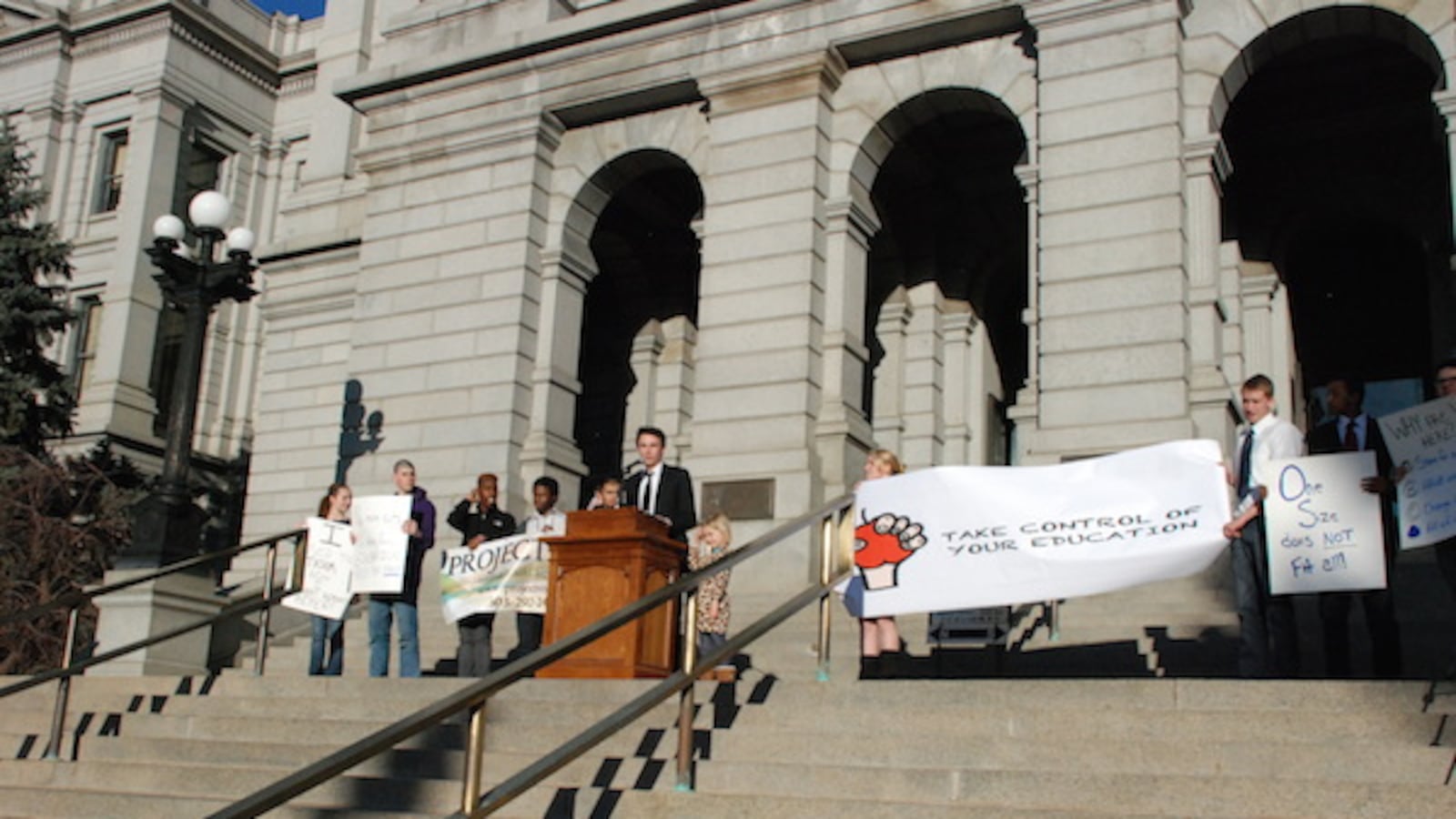 Denver Student Union member Alex Kacsh speaks from the steps of the capitol, flanked by representatives of Project Voyce and other students.