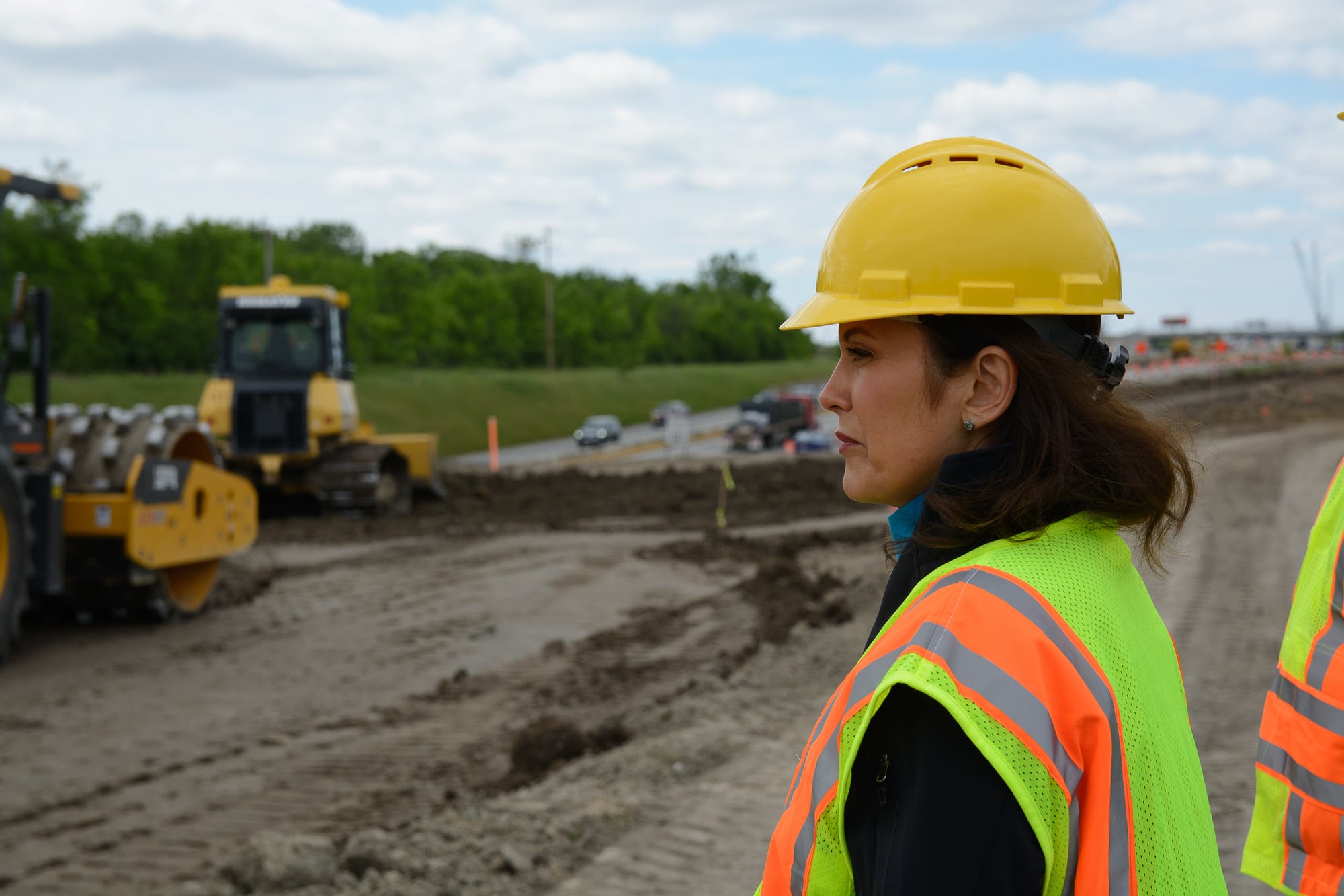 Gov. Whitmer in hard hat and vest with construction machinery in background at road building site