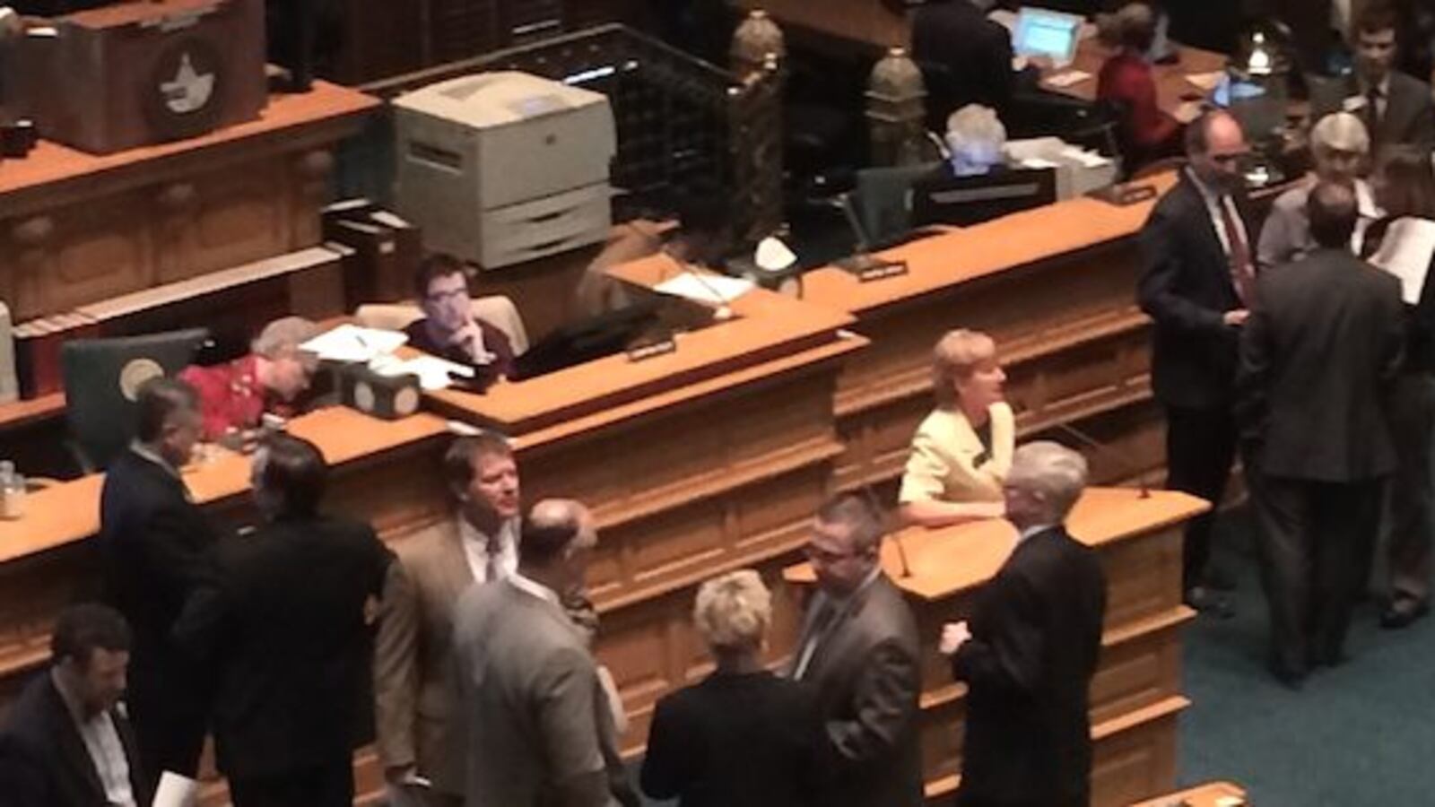 Representatives cluster around the rostrum during school funding debate.