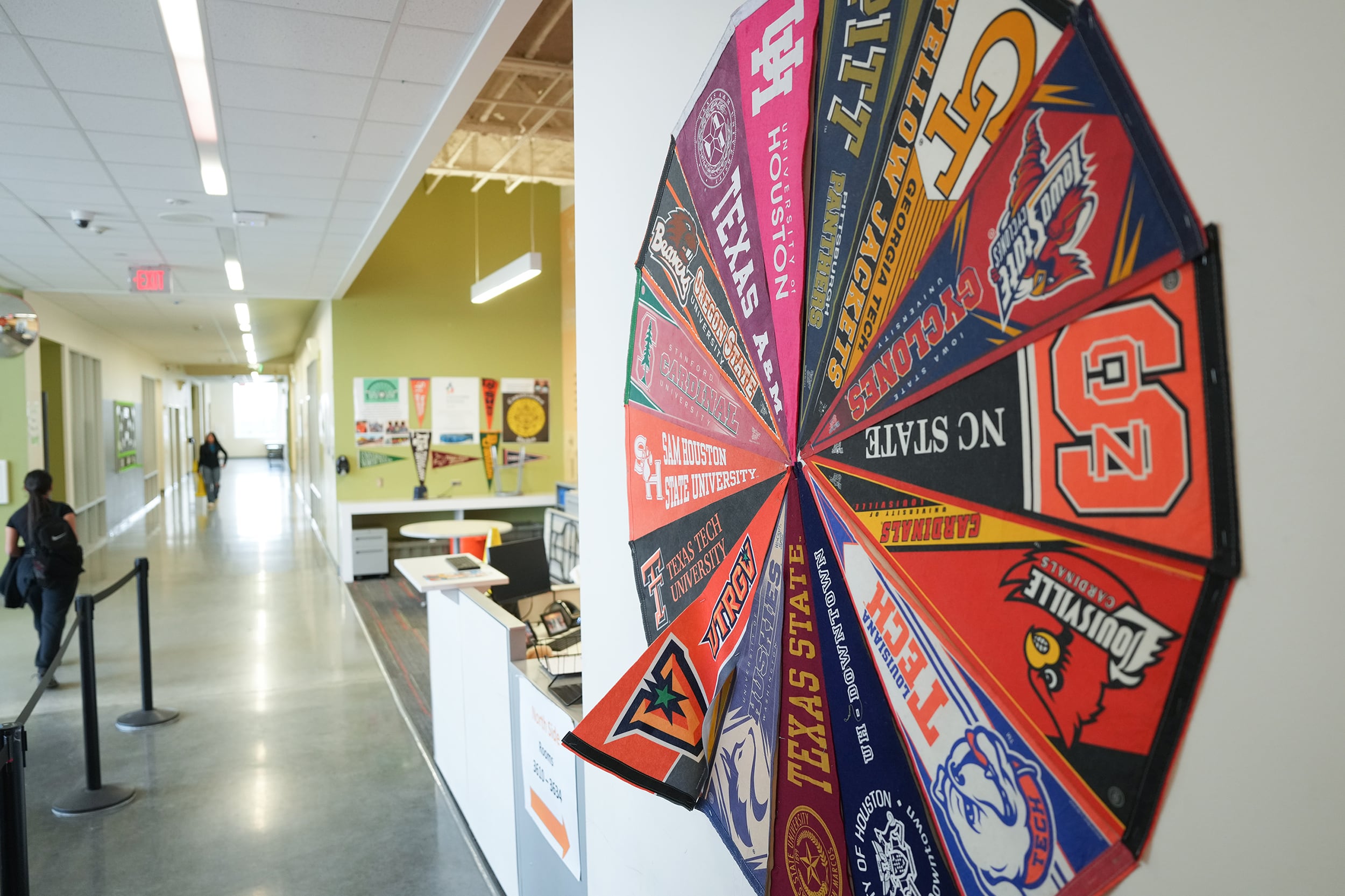 A person walks by a wall full of college pendants hanging in a circle of a school building.