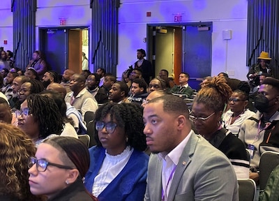 A room full of adults in business clothes sit in a conference room.