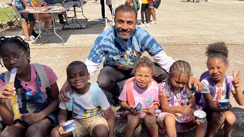 Man in blue and white tie-dye shirt poses with five young children in backpacks