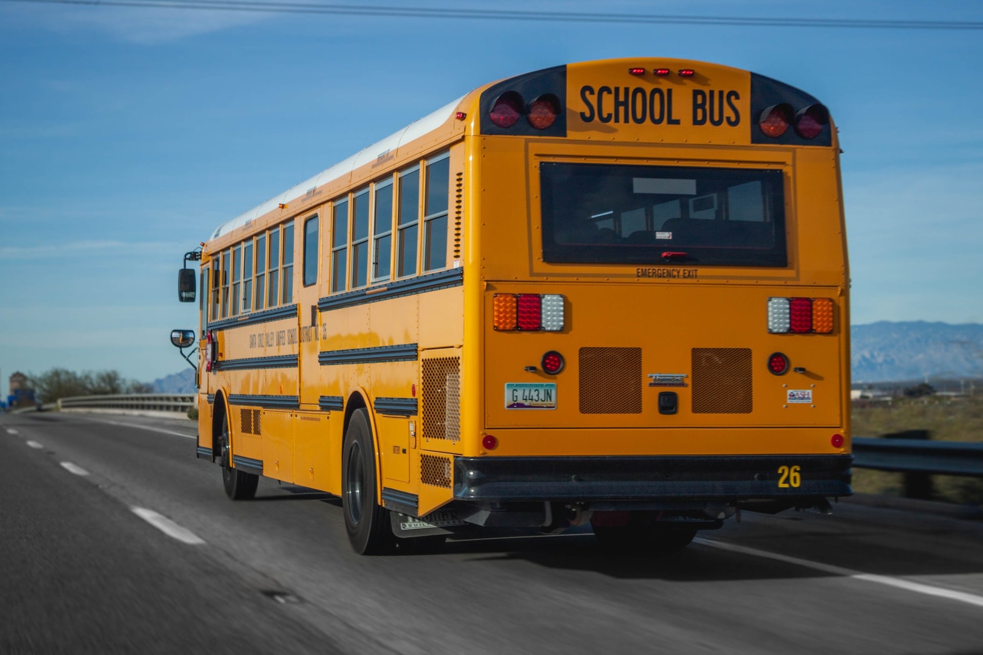 Back of a yellow school bus traveling down a road