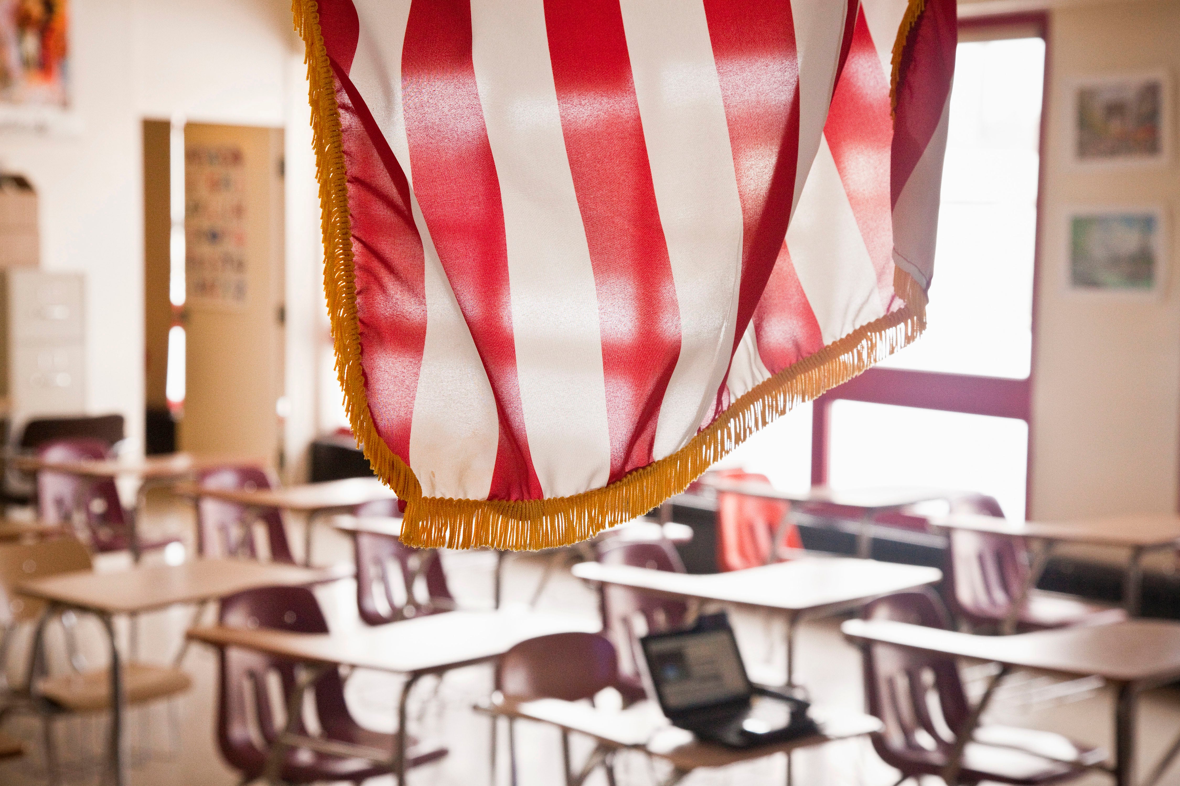 An American flag hangs in front of an empty classroom.
