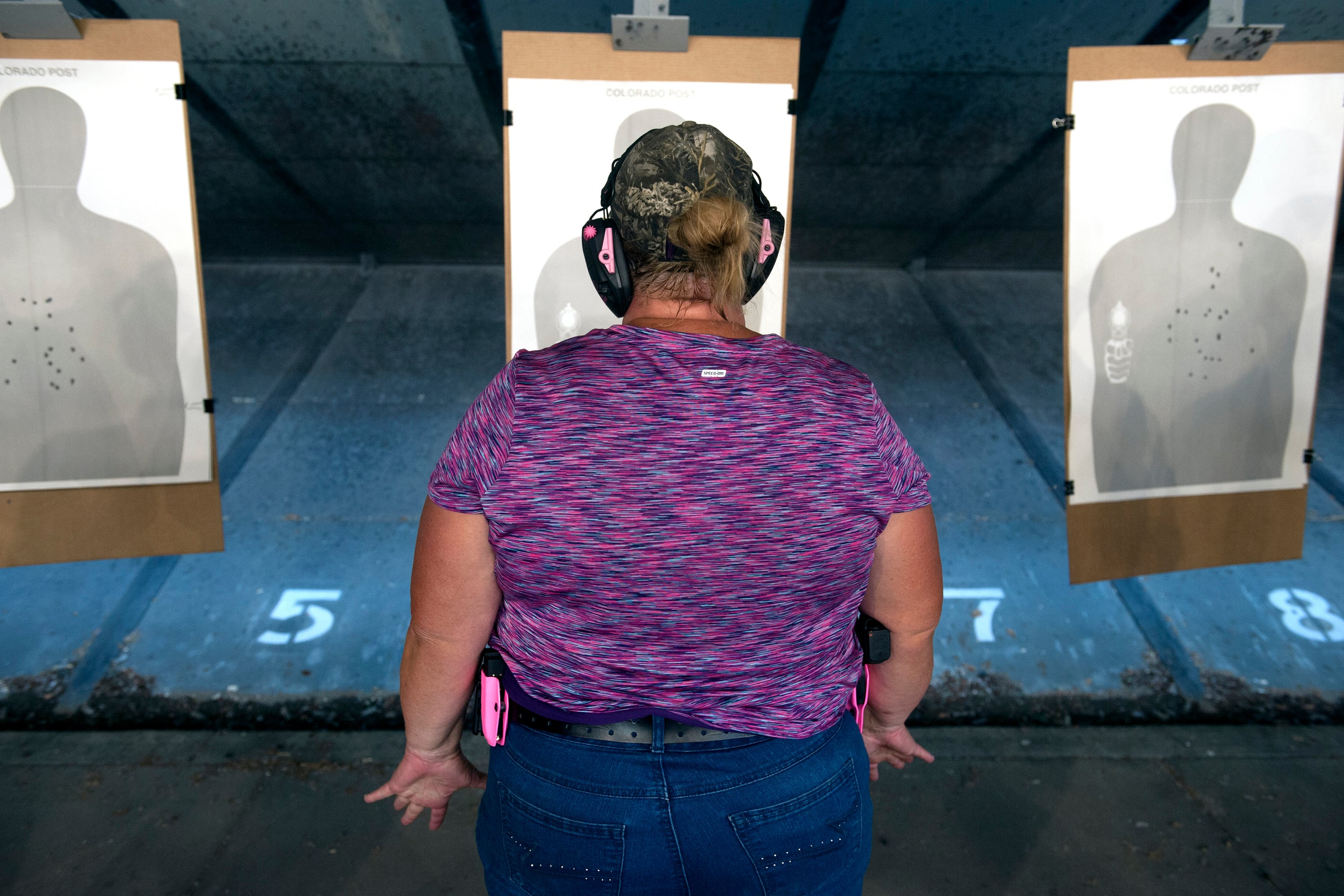 A woman wearing a purple shirt stands in front of three practice targets in a gun range.