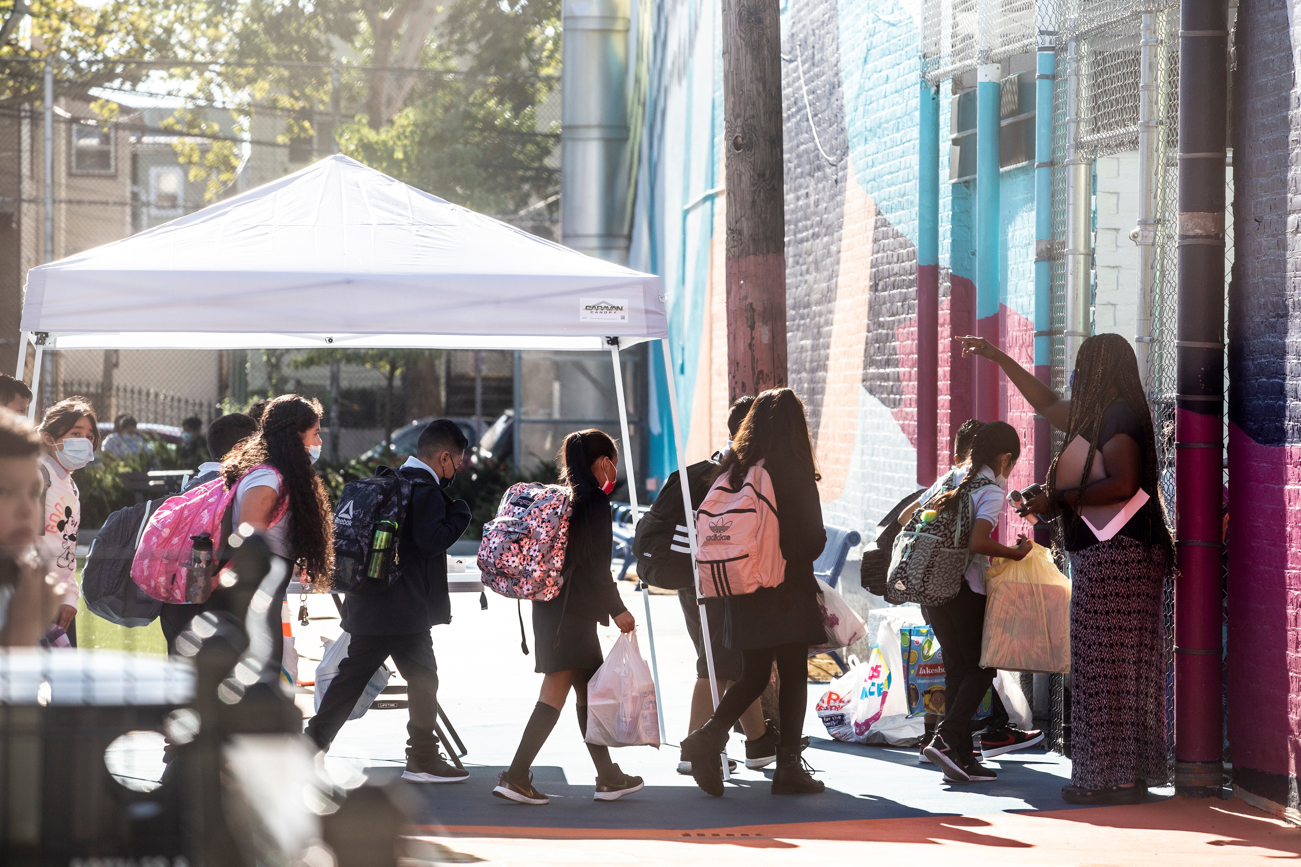 Students wearing backpacks and uniforms enter a school building one by one.