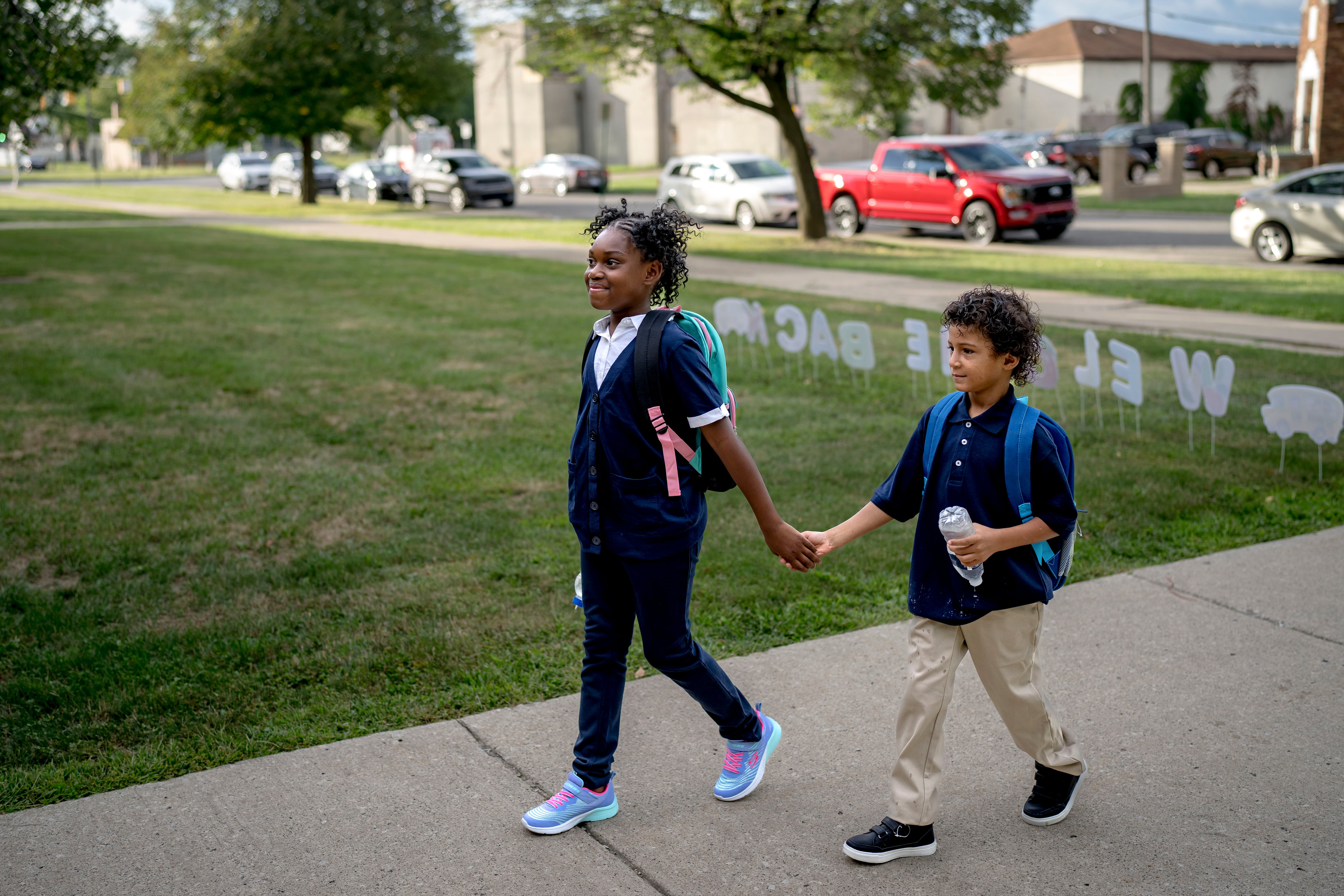 A brother and sister hold hands as they walk toward their school on the first day of classes.
