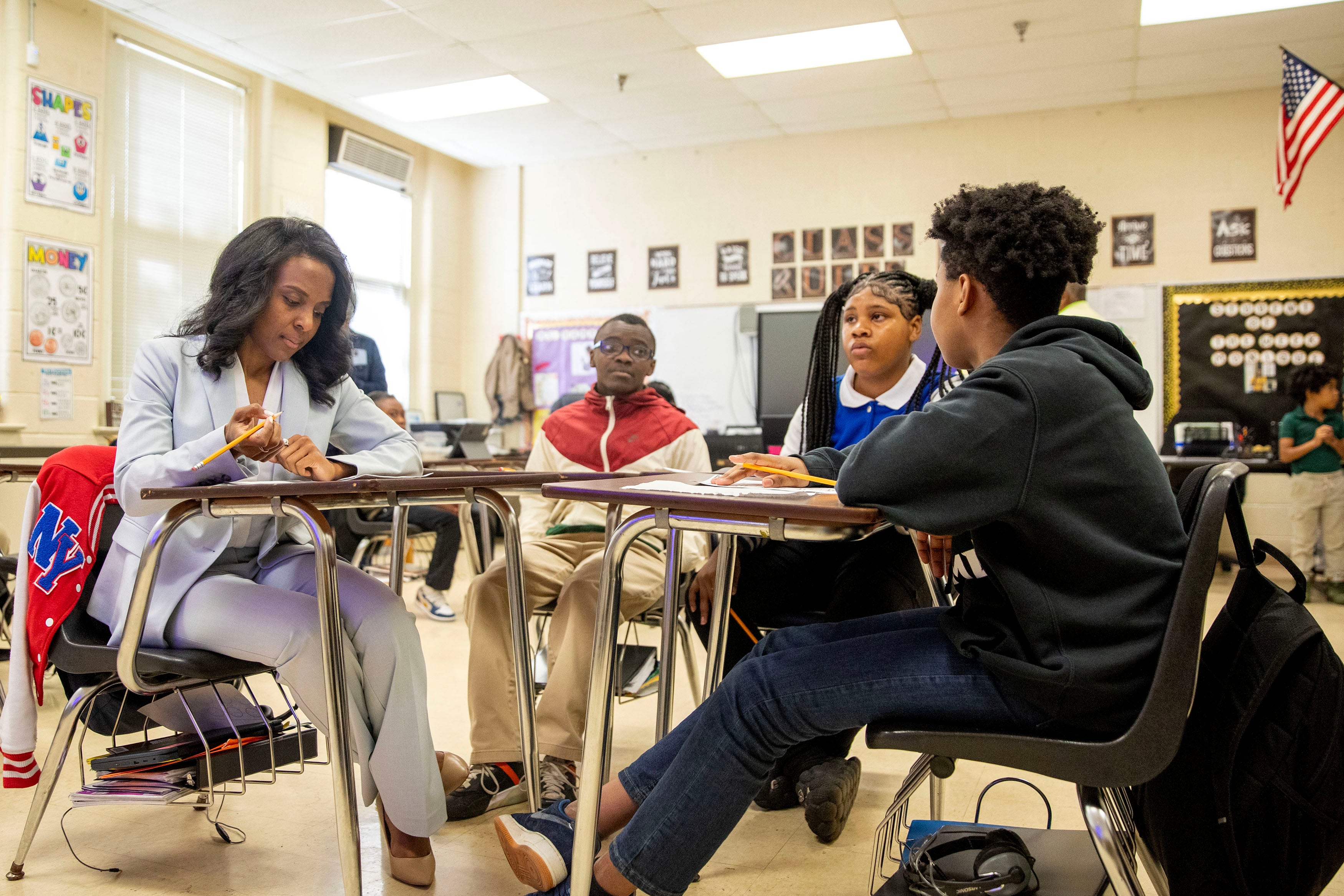 An adult and a couple of students sit at a table in a classroom.