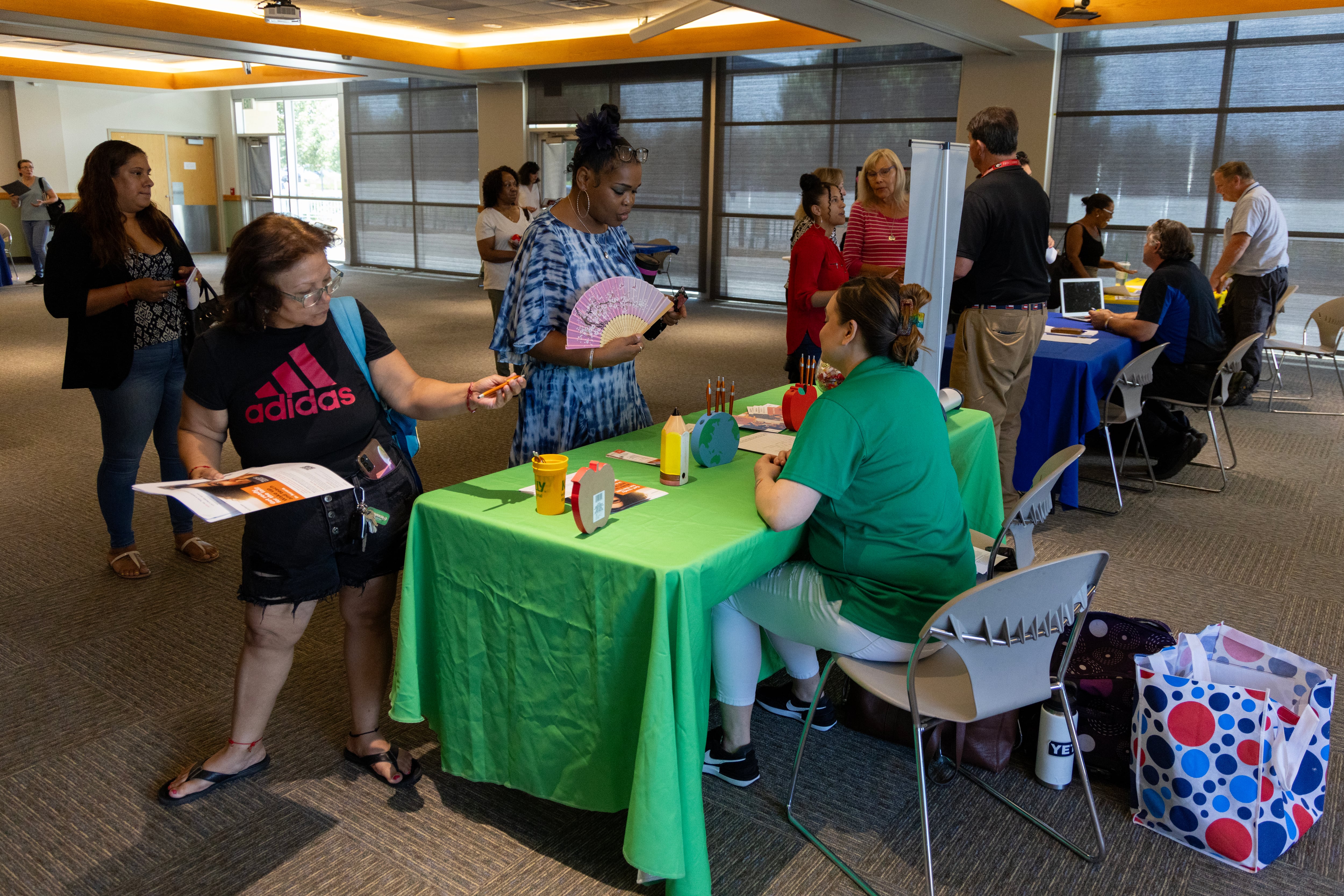 Two women stand in front of a job fair table staffed by a recruiter in a green shirt.