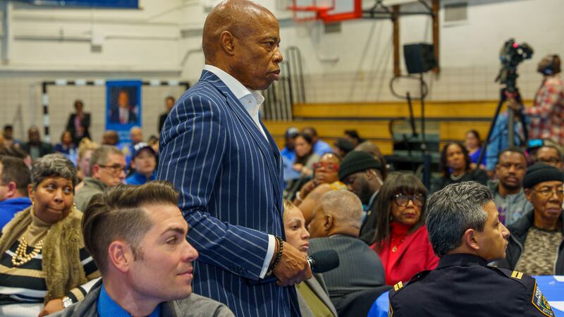 A man wearing a blue striped suit stands in a school gym full of people with a basketball hoop in the background.