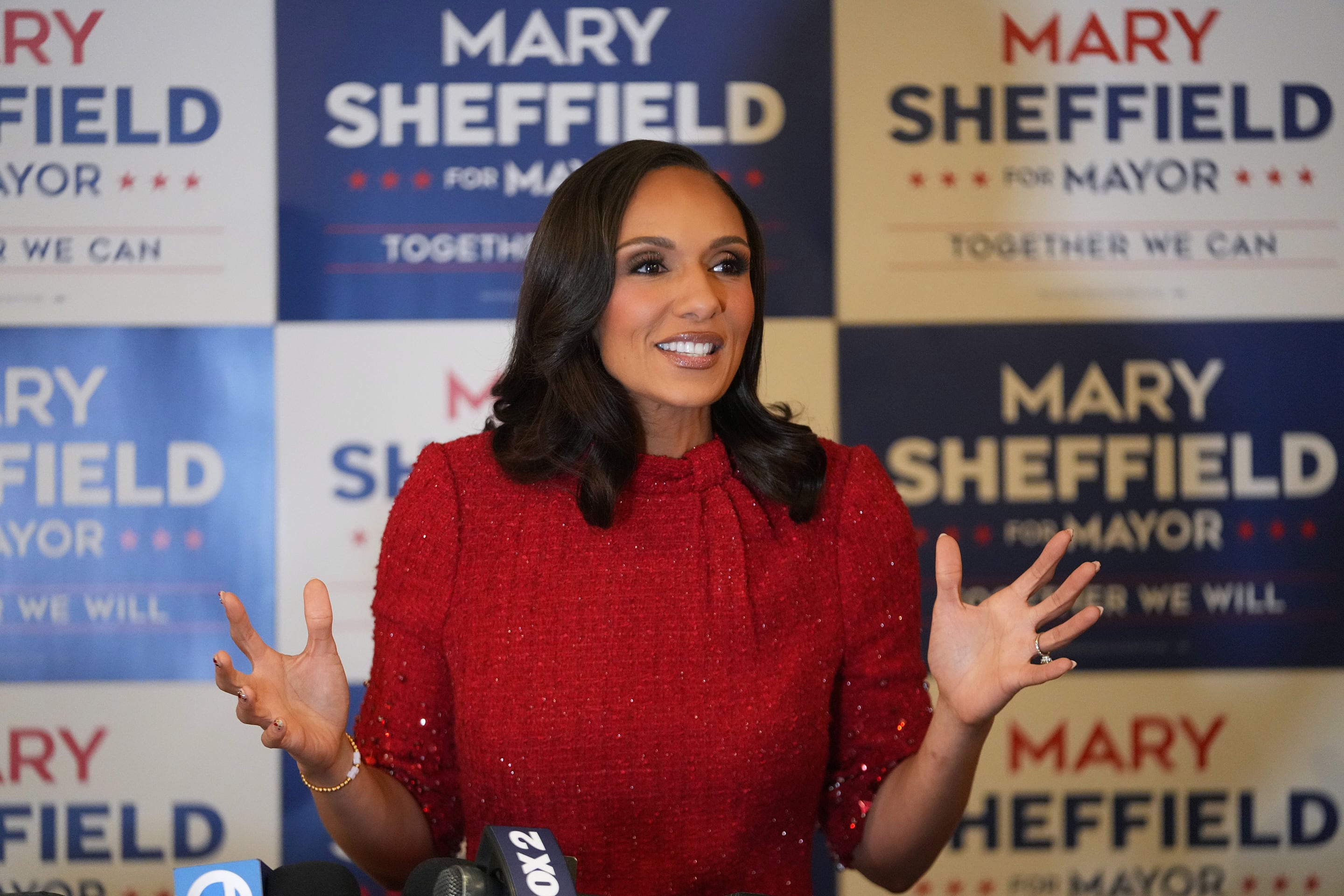 A photograph of a Black woman wearing a red dress standing in front of a wall of colorful posters.