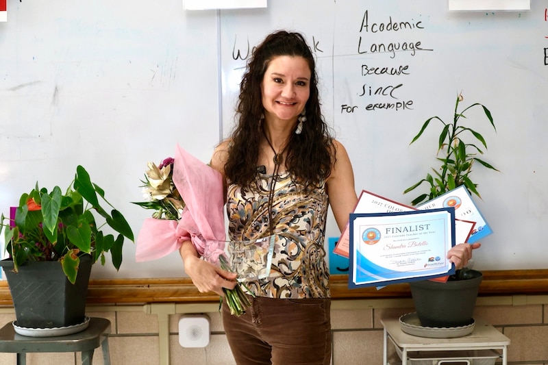 A woman with long hair holds flowers and a certificate.