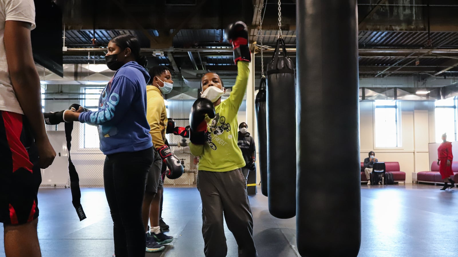 Students work on boxing and conditioning drills in a large indoor gym.