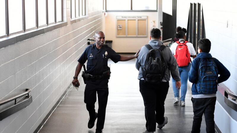A smiling school police officer interacts with students in a hallway.