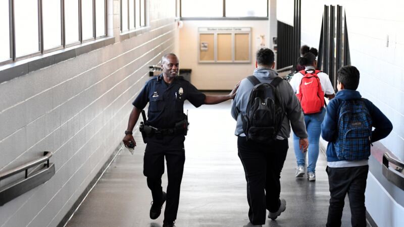 A smiling school police officer interacts with students in a hallway.