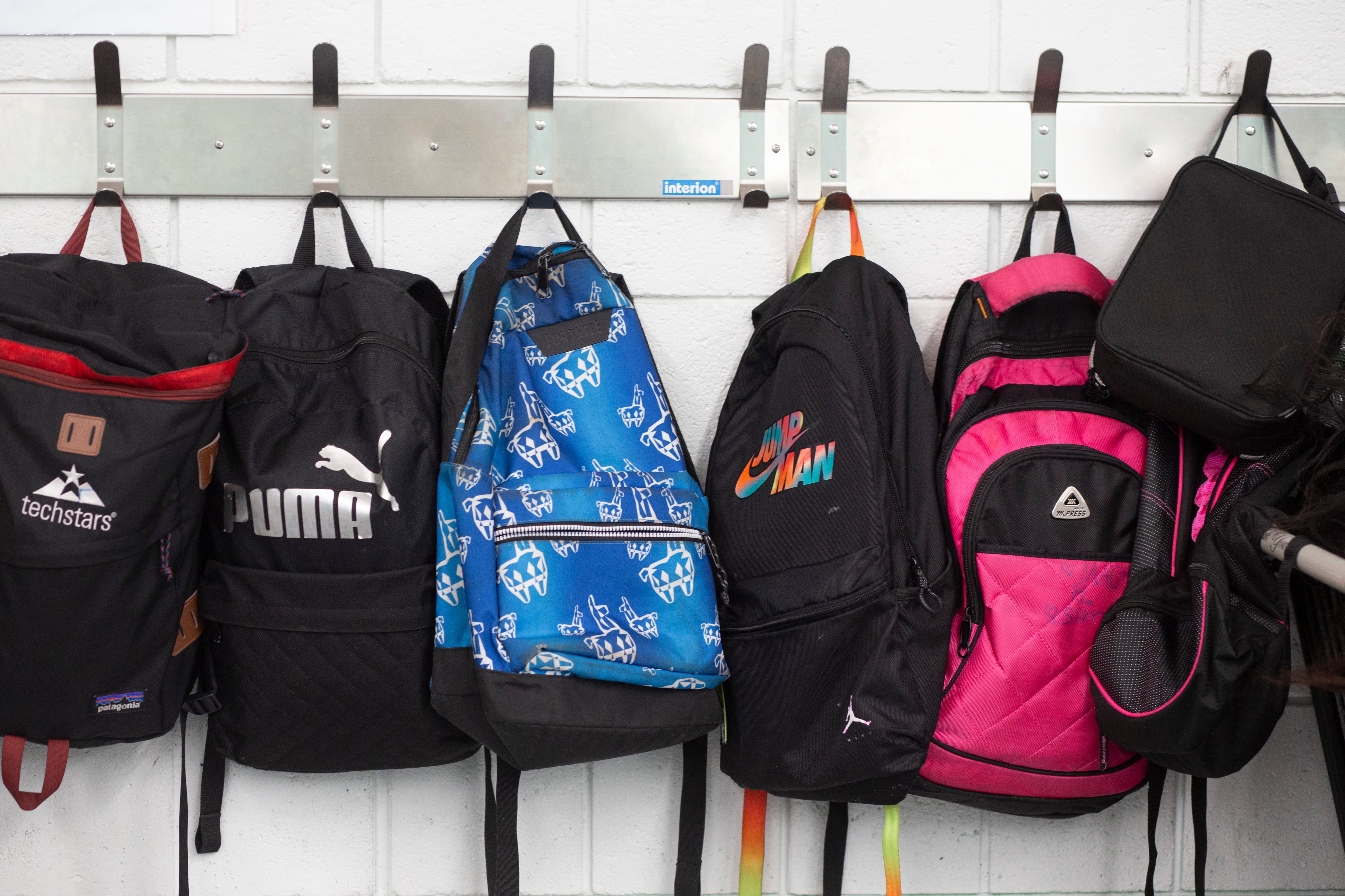 A row of backpacks hang on hooks.