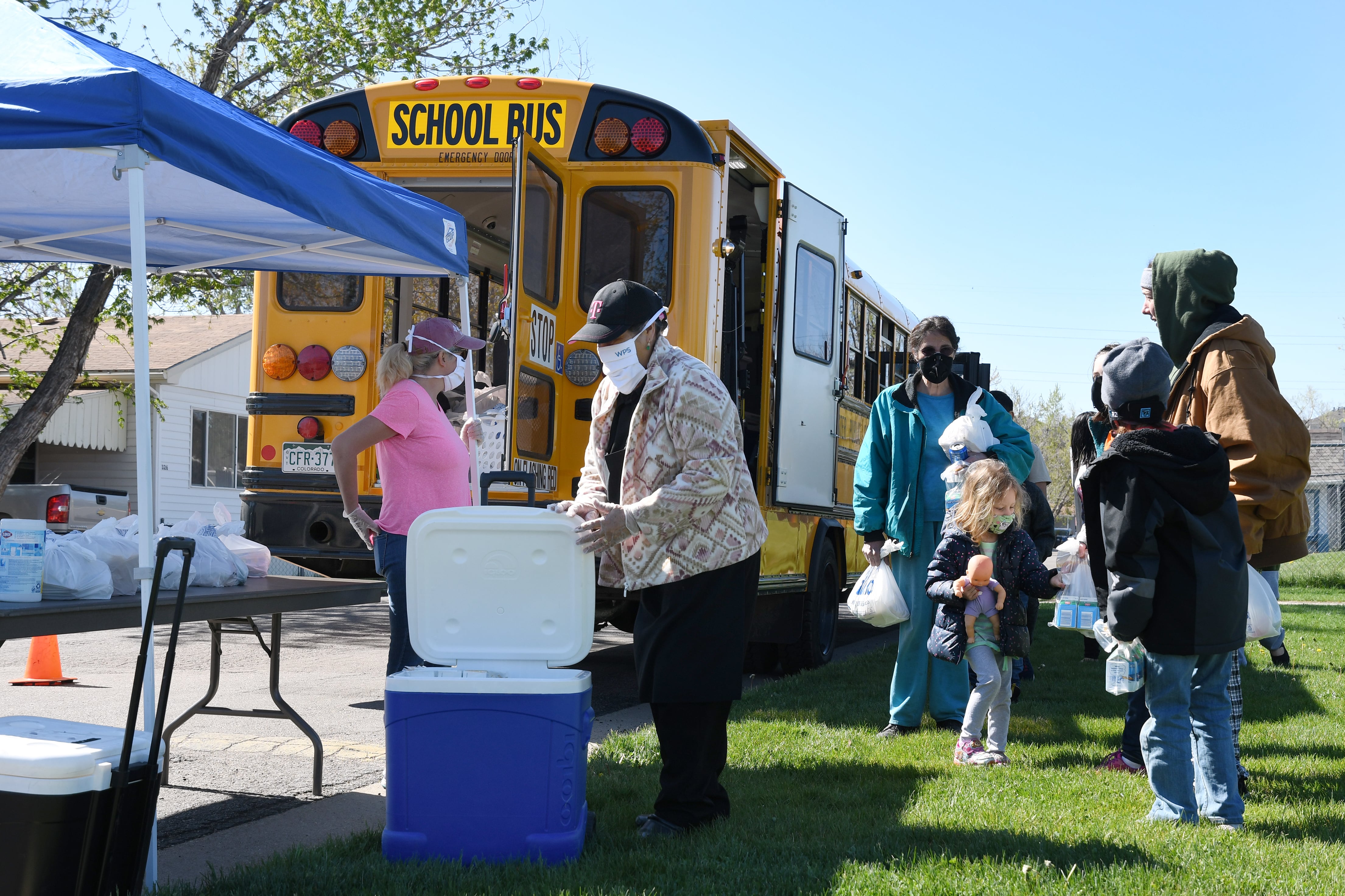 Children and adults wait for bagged food delivered by a school bus at Berkeley Village Mobile Home Park in Arvada, Colorado.