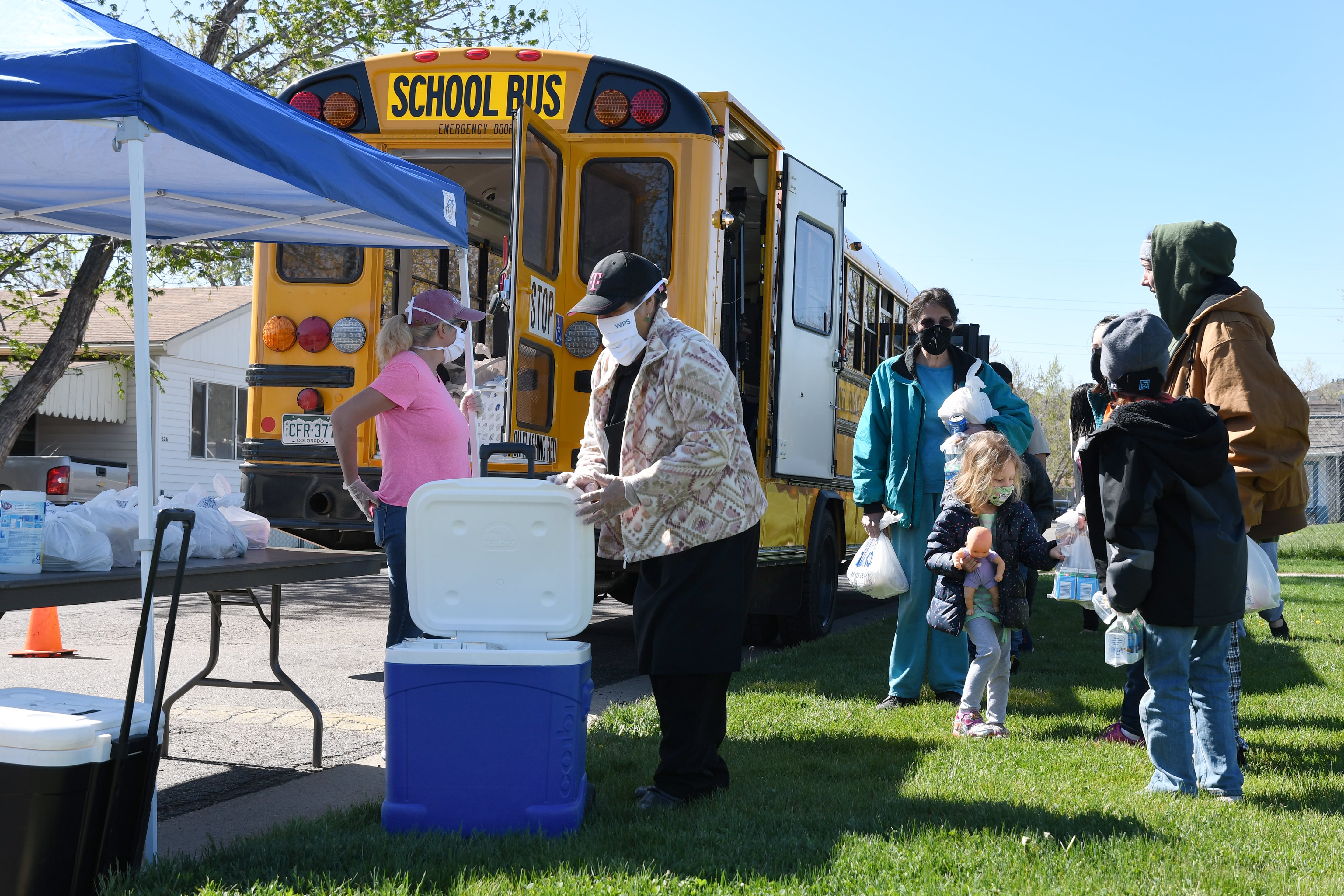 Children and adults wait for bagged food delivered by a school bus at Berkeley Village Mobile Home Park in Arvada, Colorado.