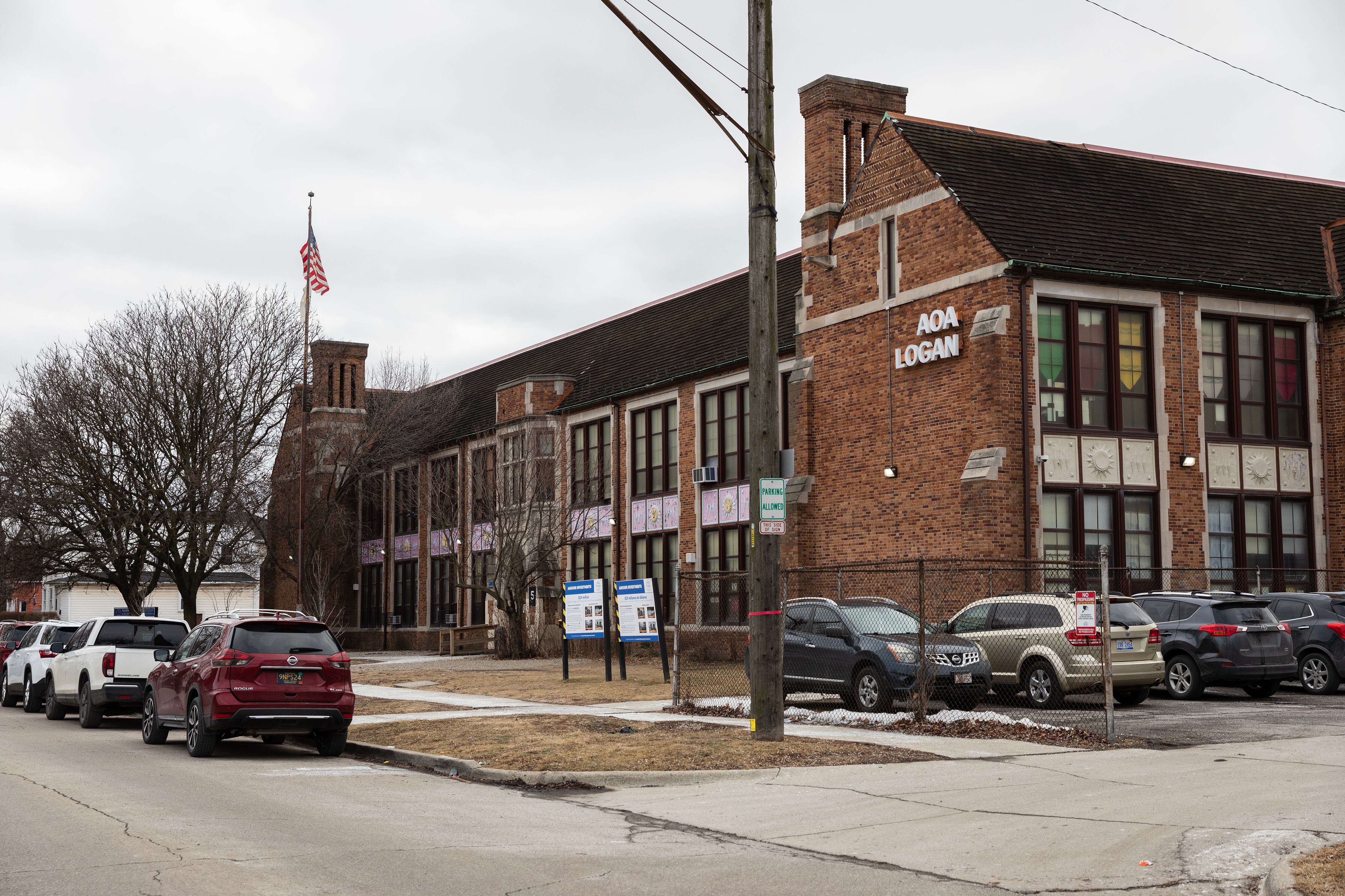 Cars line the street outside the front entrance of a large brick school building.