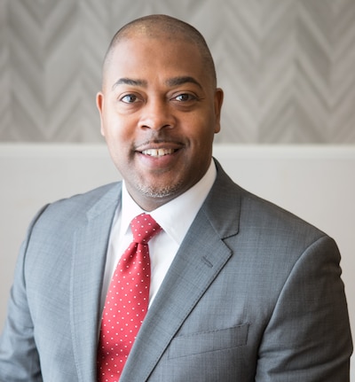 Headshot of a man wearing a dark gray suit and a red tie.