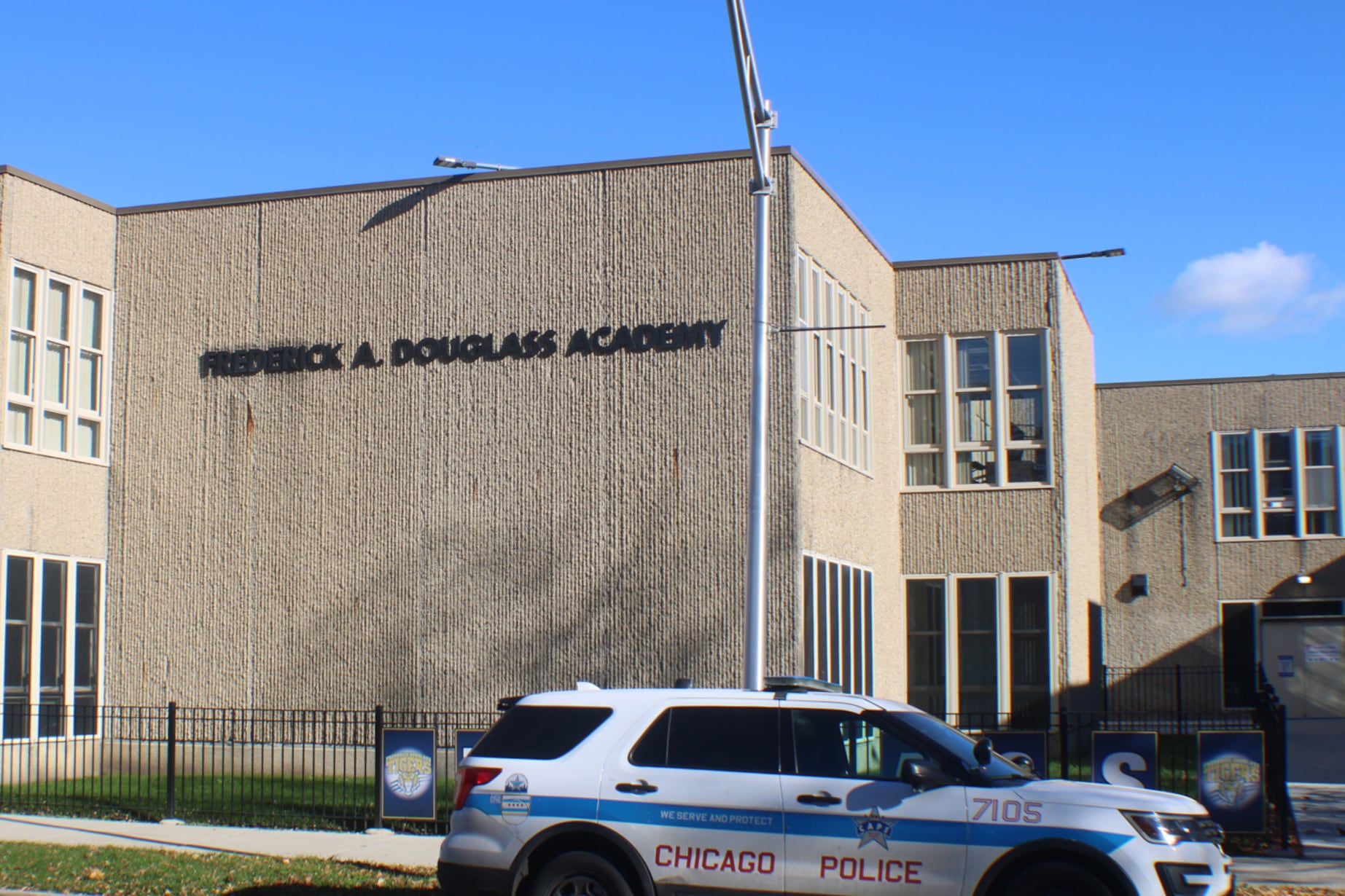 The side of a tan brick school with the name of the school on the side of the building with a Chicago Police car in the foreground.